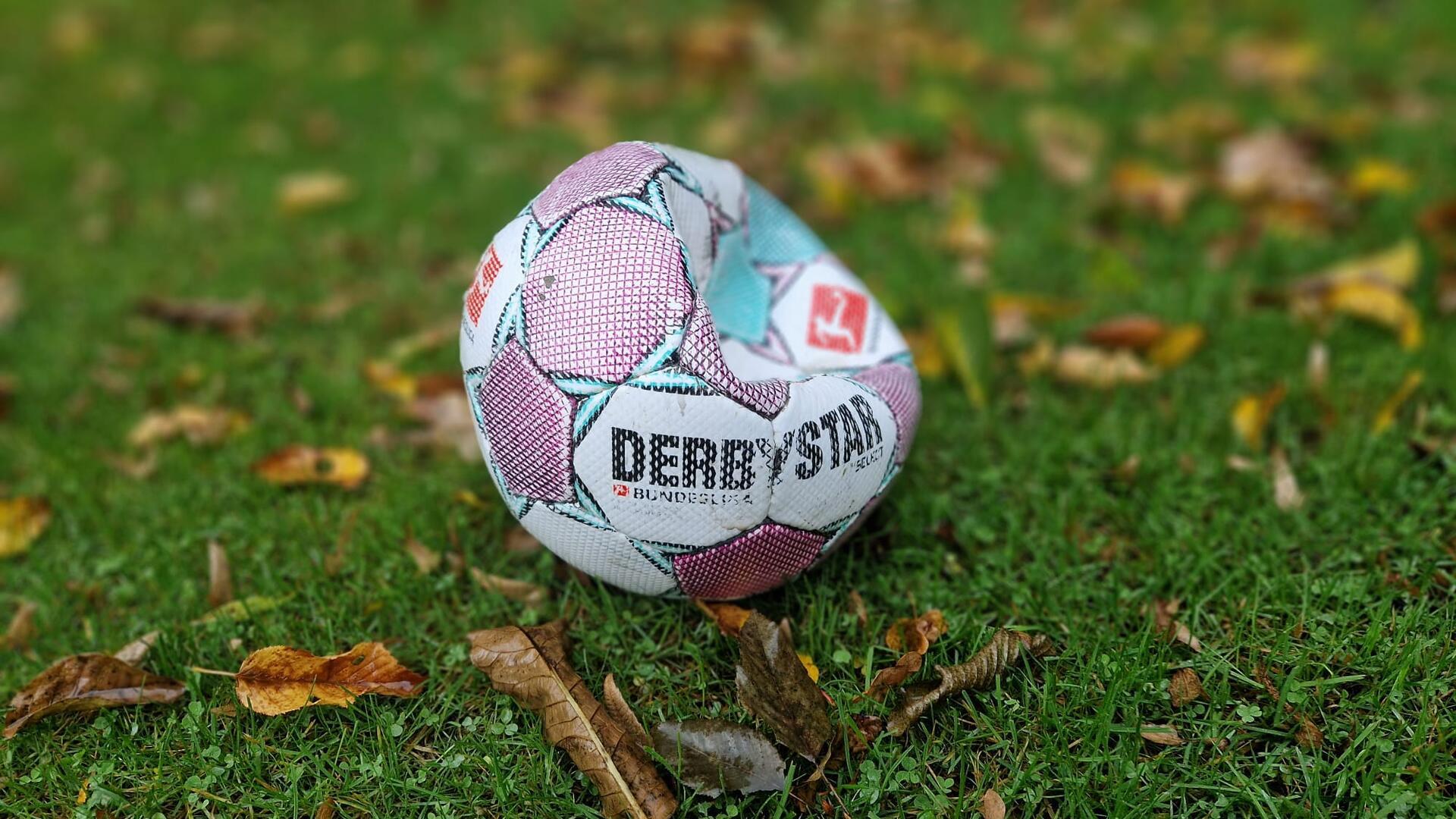 Ein kaputter Fußball mit wenig Luft liegt auf nassem Rasen.