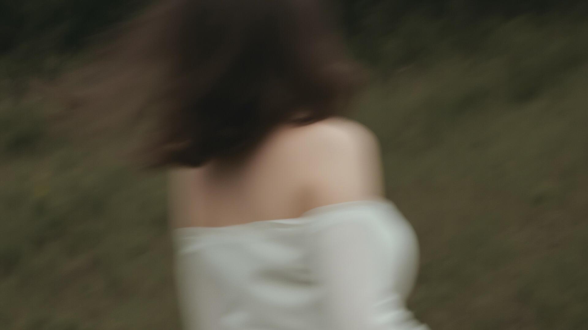 Eine junge Frau rennt in einem weißen Kleid durch den Wald. Das Bild ist verschwommen. Man erkennt de Frau schemenhaft von hinten.