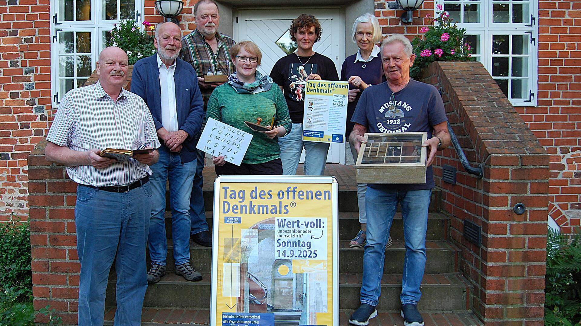 Mehrere Menschen stehen vor einem Gebäude und halten historische Gegenstände und Plakate in der Hand. 