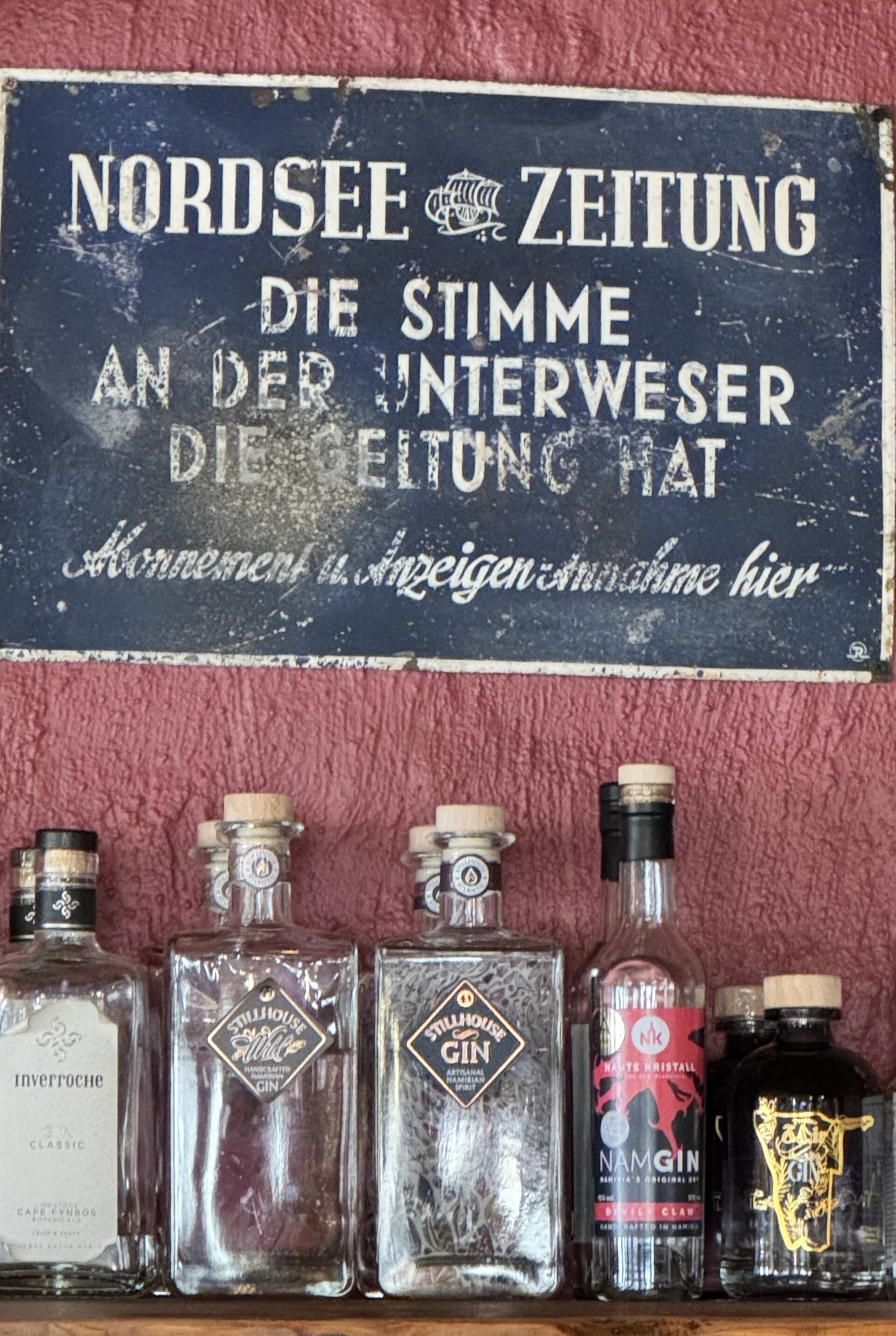 Ein Schild hängt über Glasflaschen, die auf einem Regal stehen, an der Wand.