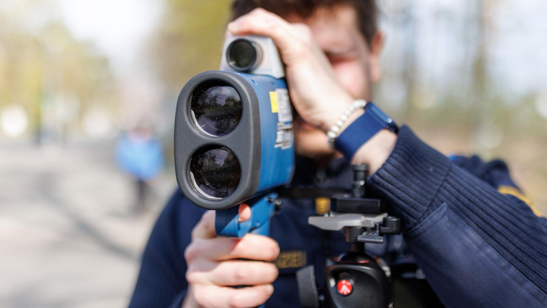  Ein Polizist misst mit einem Lasermessgerät die Geschwindigkeit von Verkehrsteilnehmern 