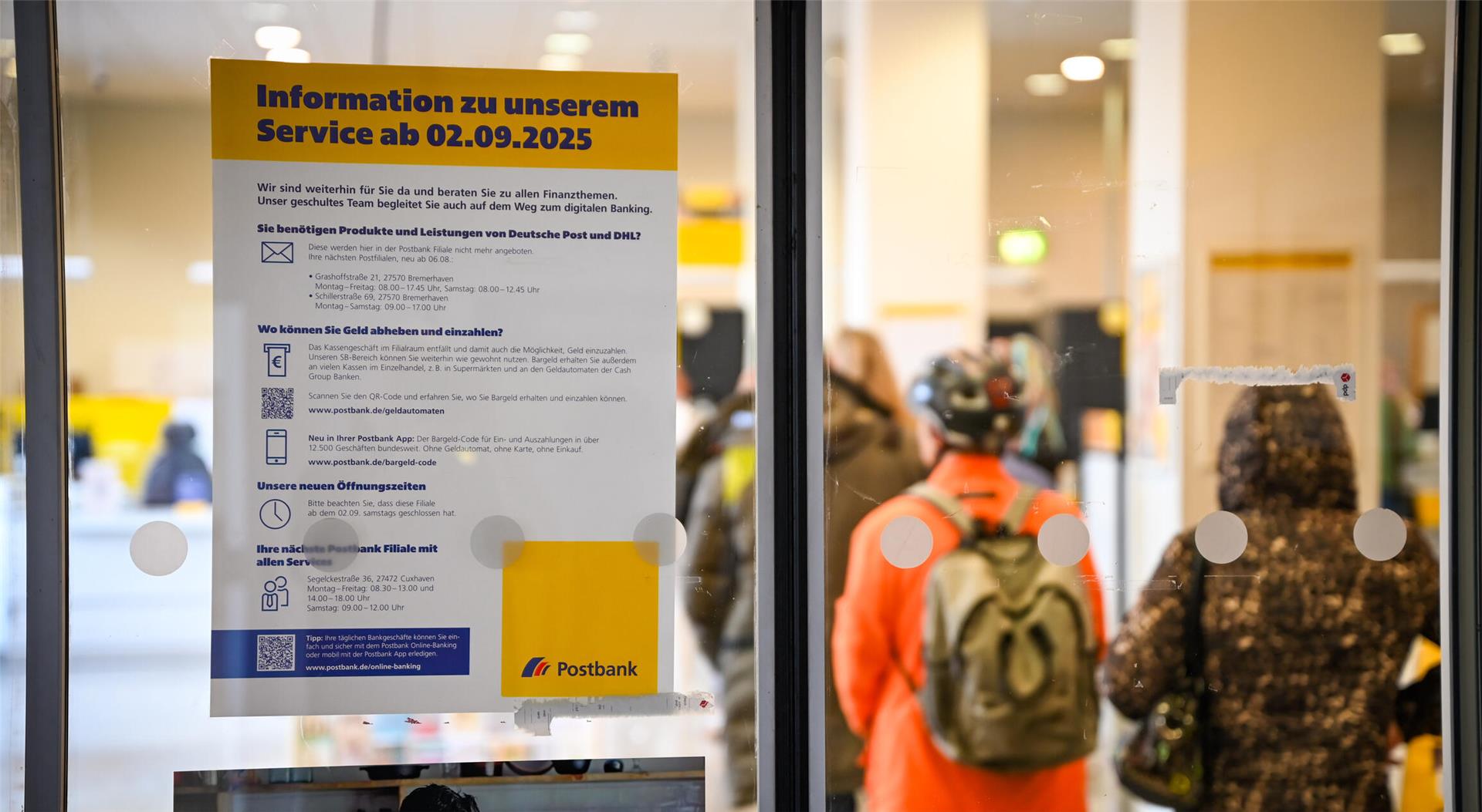 Ein Foto mit einer Menschenschlange, die am Postschalter ansteht. An einer Glastür hängt ein Zettel mit der Aufschrift: "Informationen zu unserem Service ab 02.09.2025."