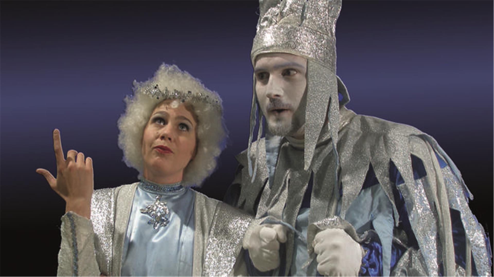 Zwei Schauspieler in silberfarbenen Kostümen stehen auf einer Bühne. 