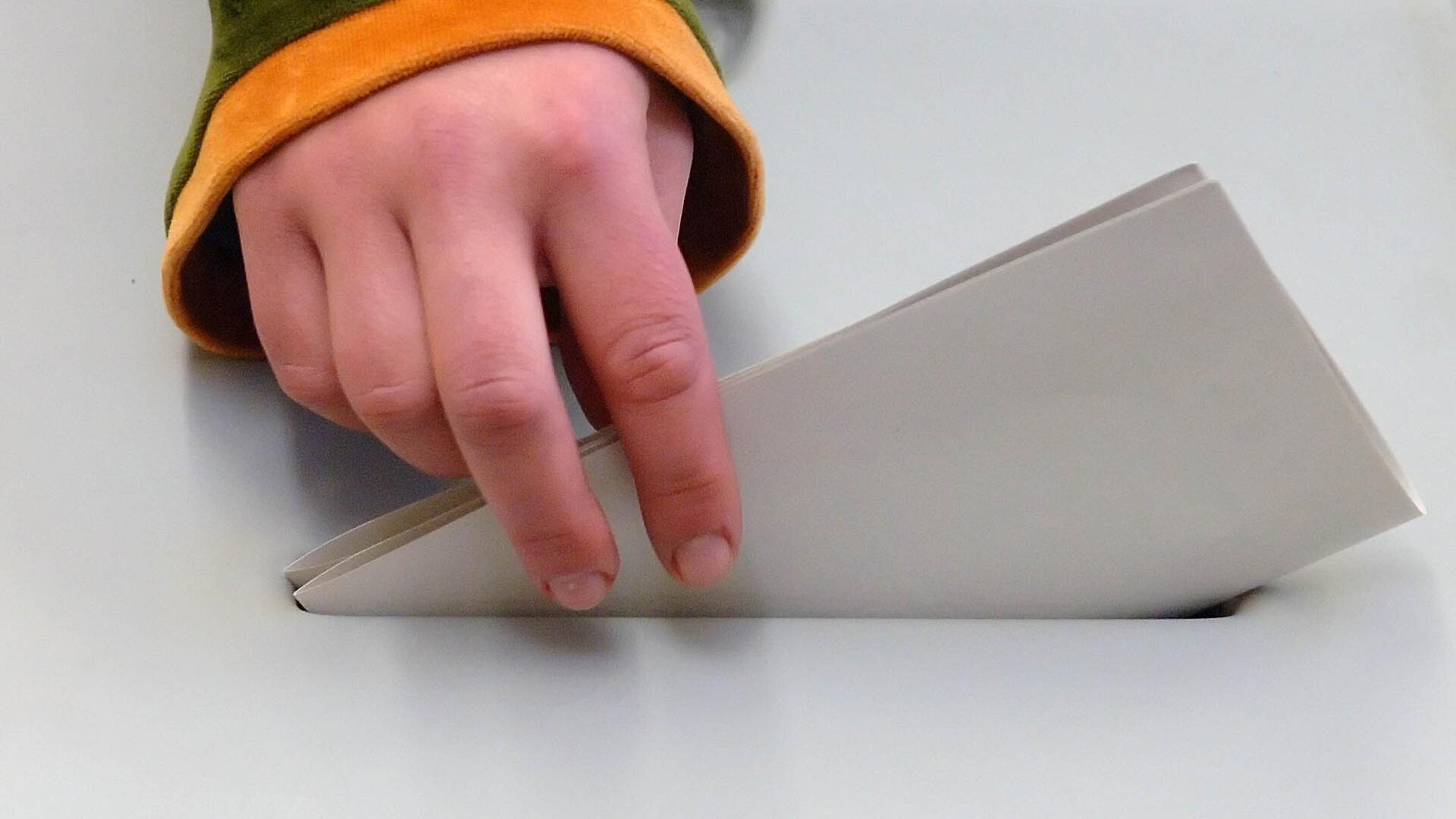 Eine Hand steckt einen Stimmzettel in die Wahlurne