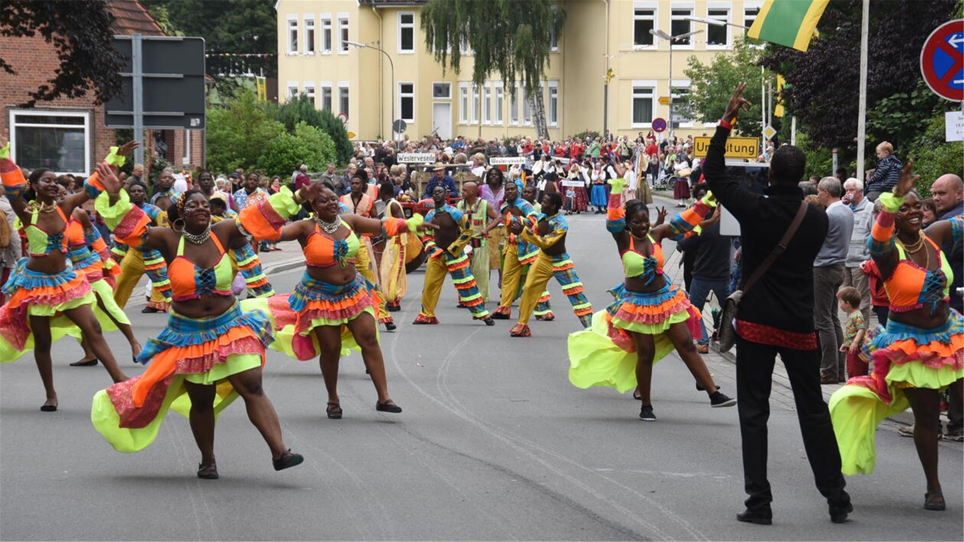Tanzgruppe in bunten Kostümen zieht beim internationalen Trachtenfest durch eine Straße, begleitet von Musik und jubelnden Zuschauern am Straßenrand.
