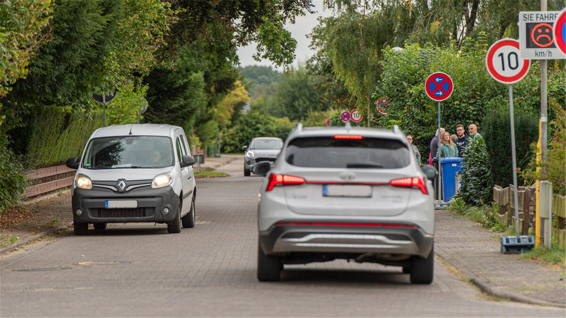 Eine Straße, auf der Autos fahren. Im Hintergrund ist ein Tempo-10-Schild zu sehen. Außerdem ein Tempotafel mit einem traurigen Smiley.