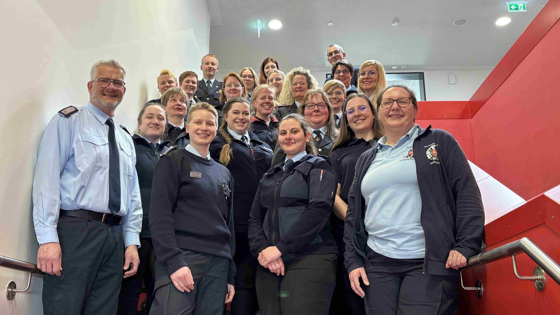 Rund 20 Feuerwehrleute in Dienstkleidung, überwiegend Frauen, stehen auf einer Treppe und blicken in die Kamera.