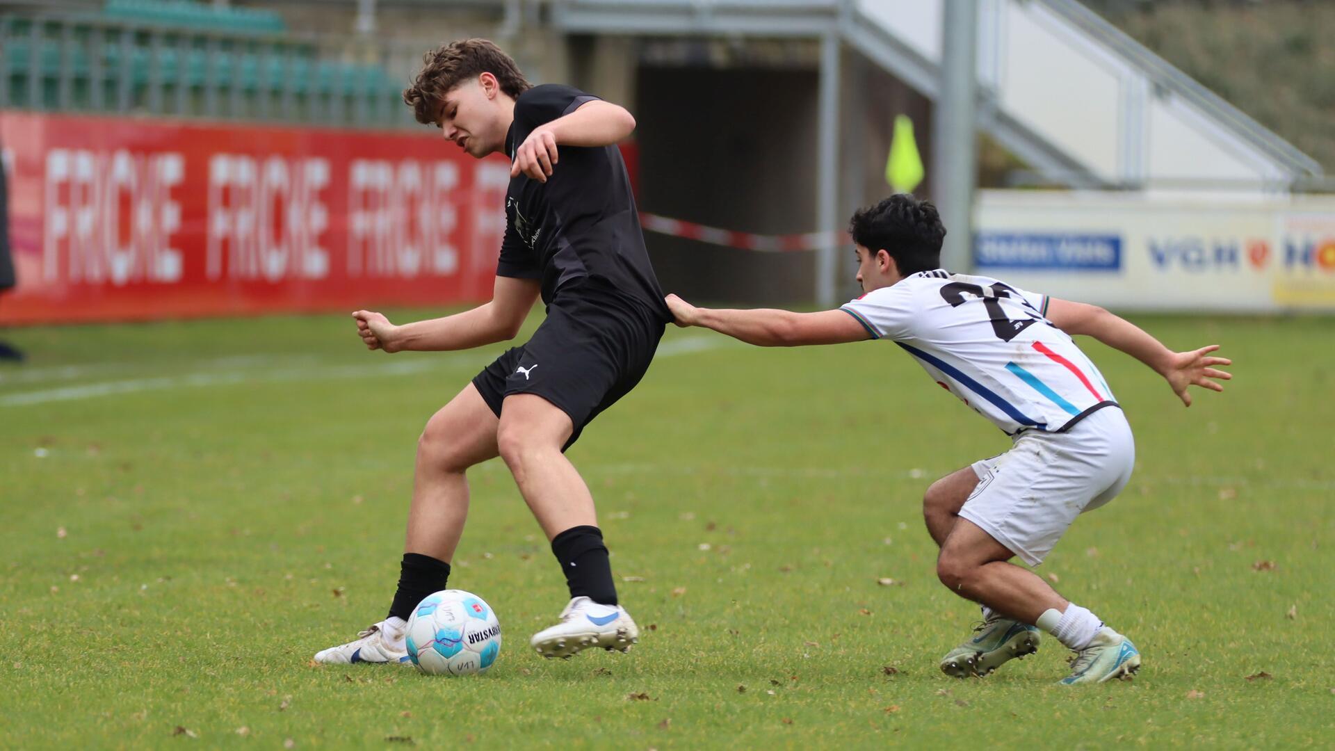 Zwei junge Männer in Sporttrikots kämpfen um einen Ball.
