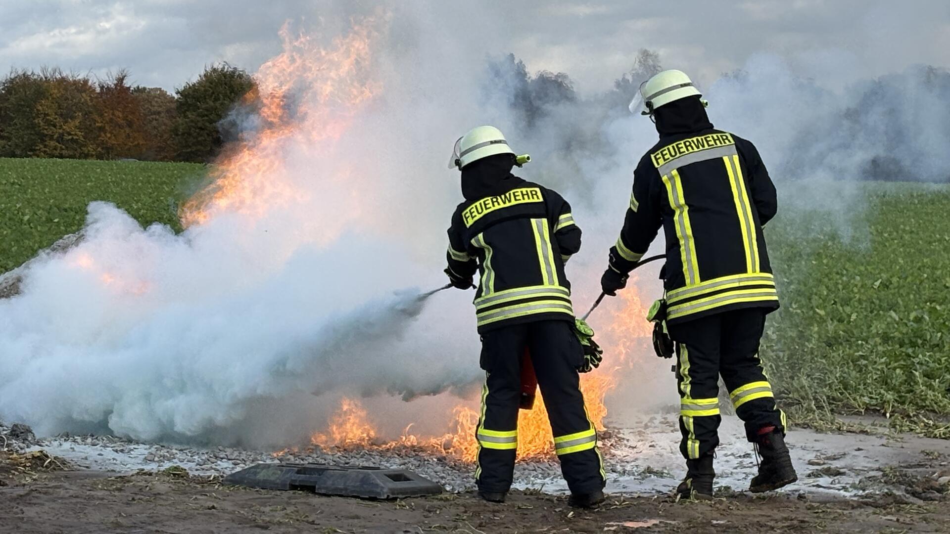 Feuerwehrleute richten einen Löschstrahl auf einen Brand an einem Feldrand. 