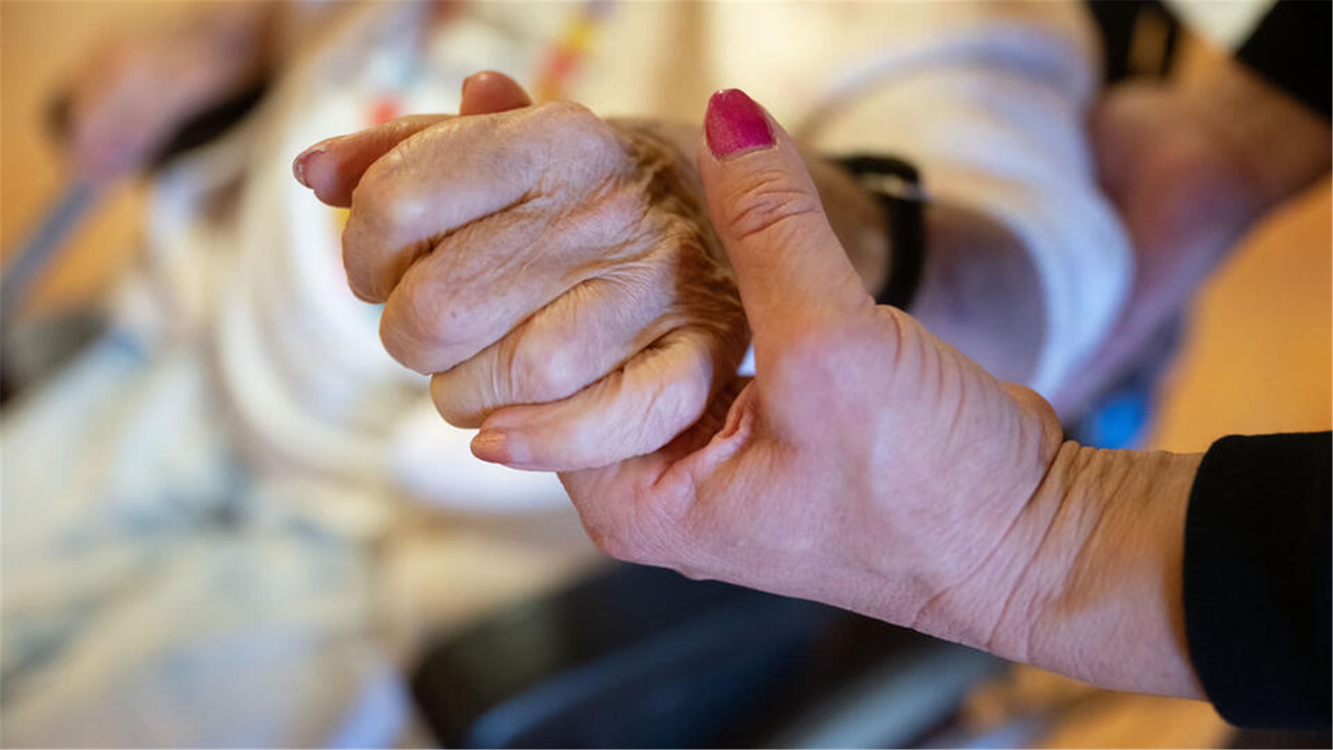 Eine Physiotherapeutin hält die Hand einer Pflegeheimbewohnerin. 