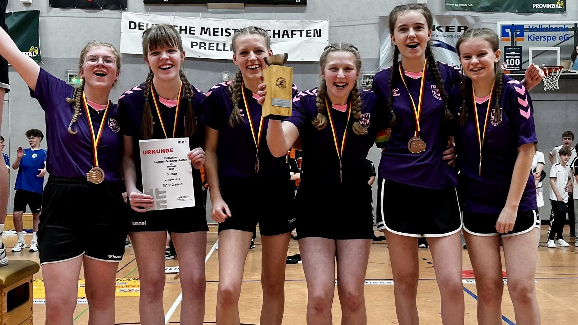 Drei Mädchen haben Medaillen um den Hals und jubeln in die Kamera.