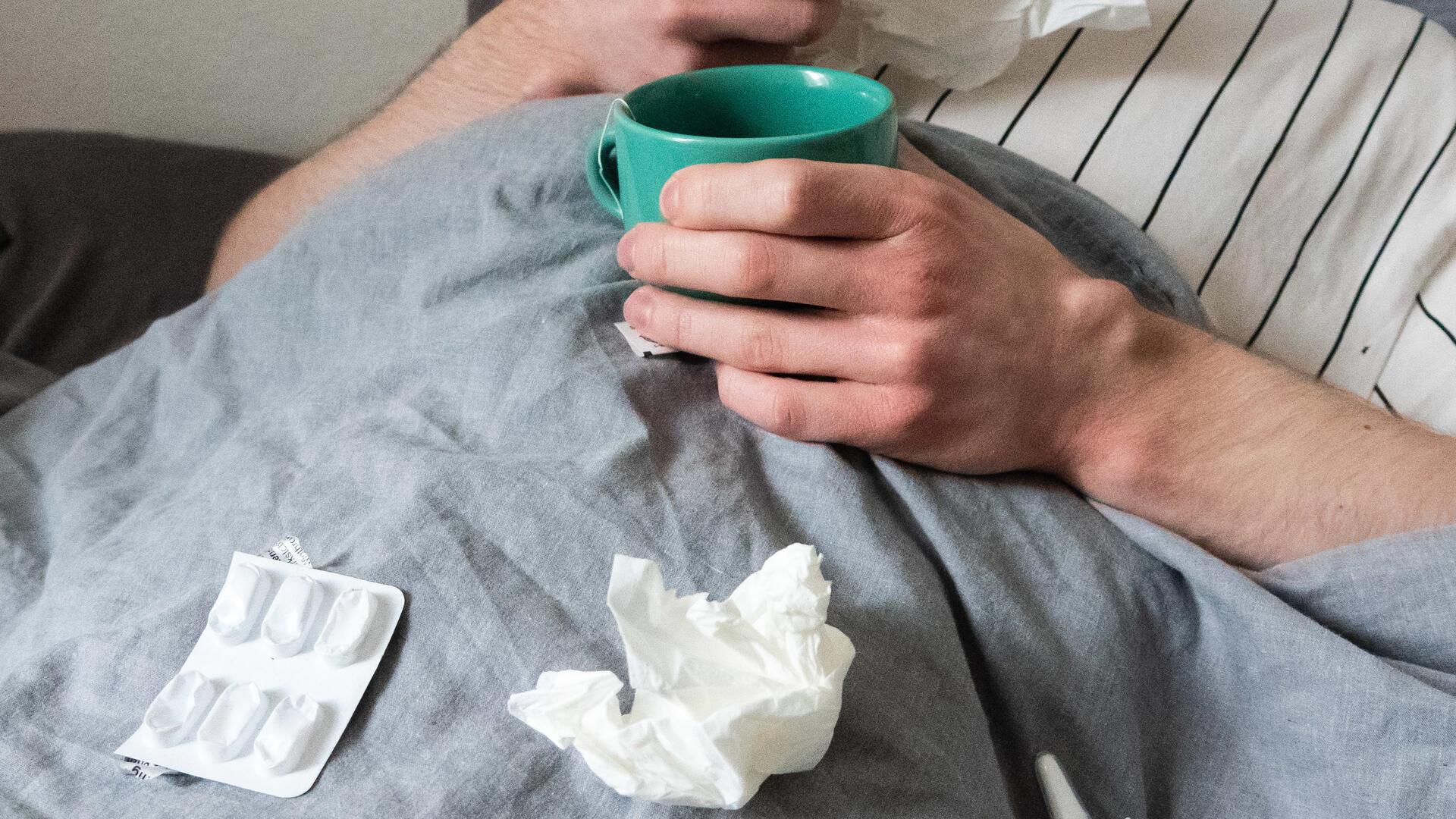  Ein Mann liegt mit Taschentüchern, Teetasse, Nasenspray und Tabletten im Bett (gestellte Szene). 