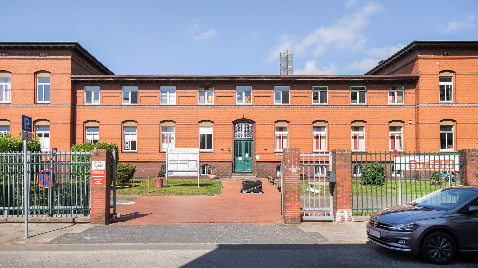 rotes Backsteingebäude mit grüner Tür in einer parkähnlichen Anlage 