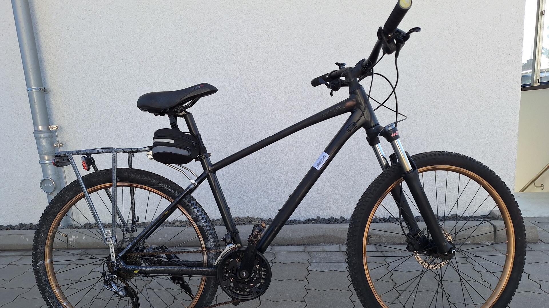 Ein schwarzes Fahrrad mit goldfarbenen Felgen steht vor einer weißen Wand. 