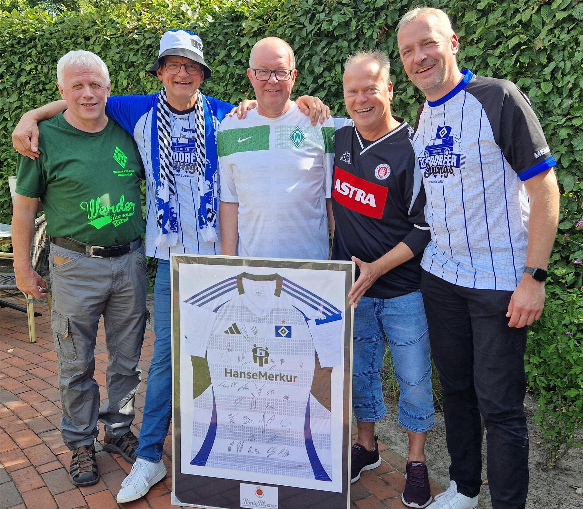 Fünf Männer stehen nebeneinander, halten ein gerahmtes HSV-Trikot fest und lächeln in die Kamera.
