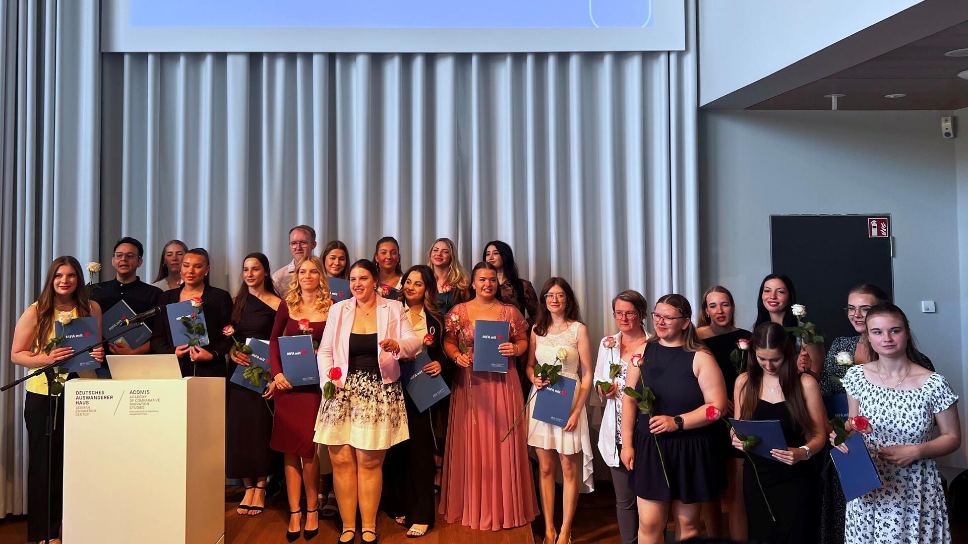 Gruppenfoto von 31 frisch freigesprochenen Medizinischen Fachangestellten in festlicher Kleidung, mit Urkunden und Rosen, aufgenommen im Deutschen Auswandererhaus Bremerhaven.