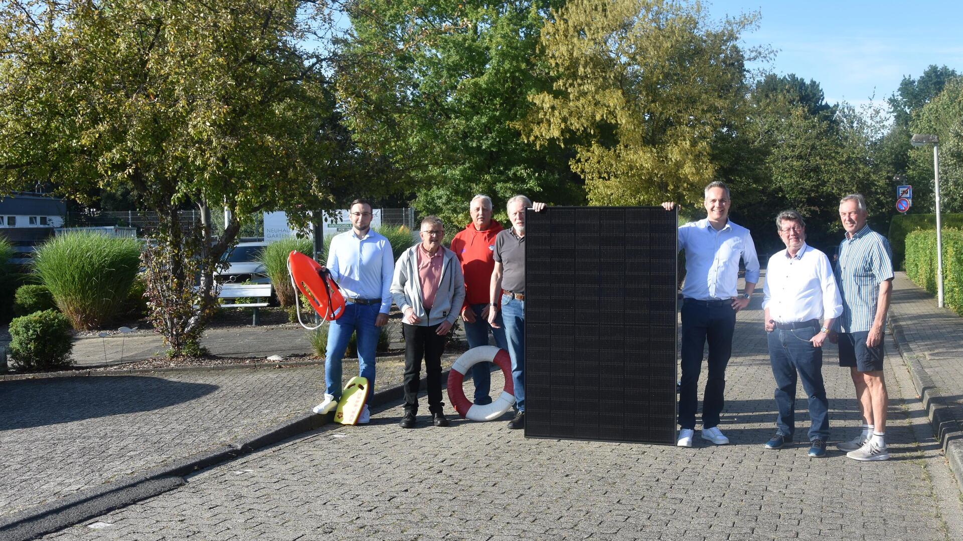 Sieben Männer stehen auf einer gepflasterten Straße und halten ein Photovoltaik-Modul in ihrer Mitte.