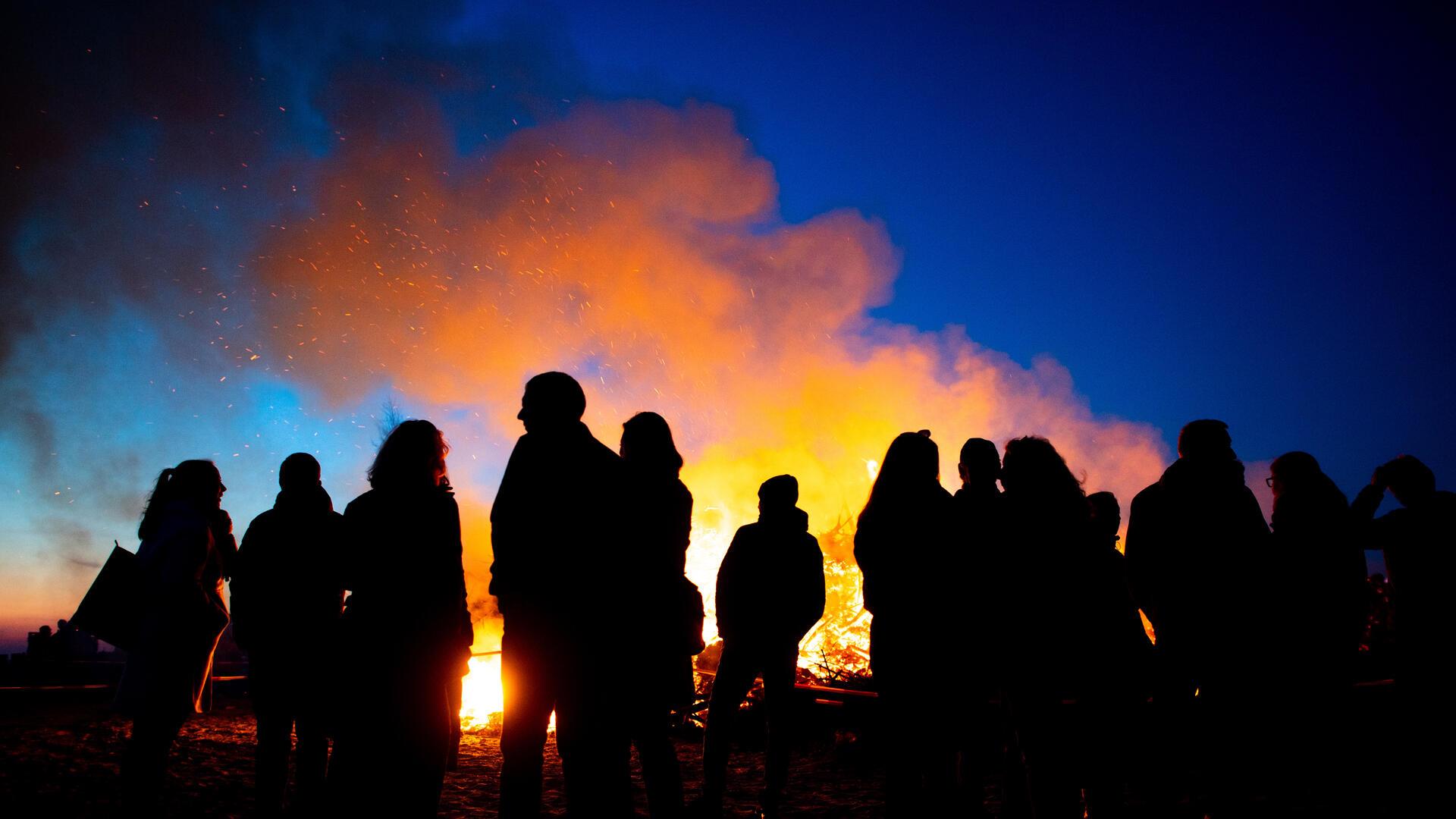 Menschen stehen vor einem Osterfeuer bei abendlichem Himmel.
