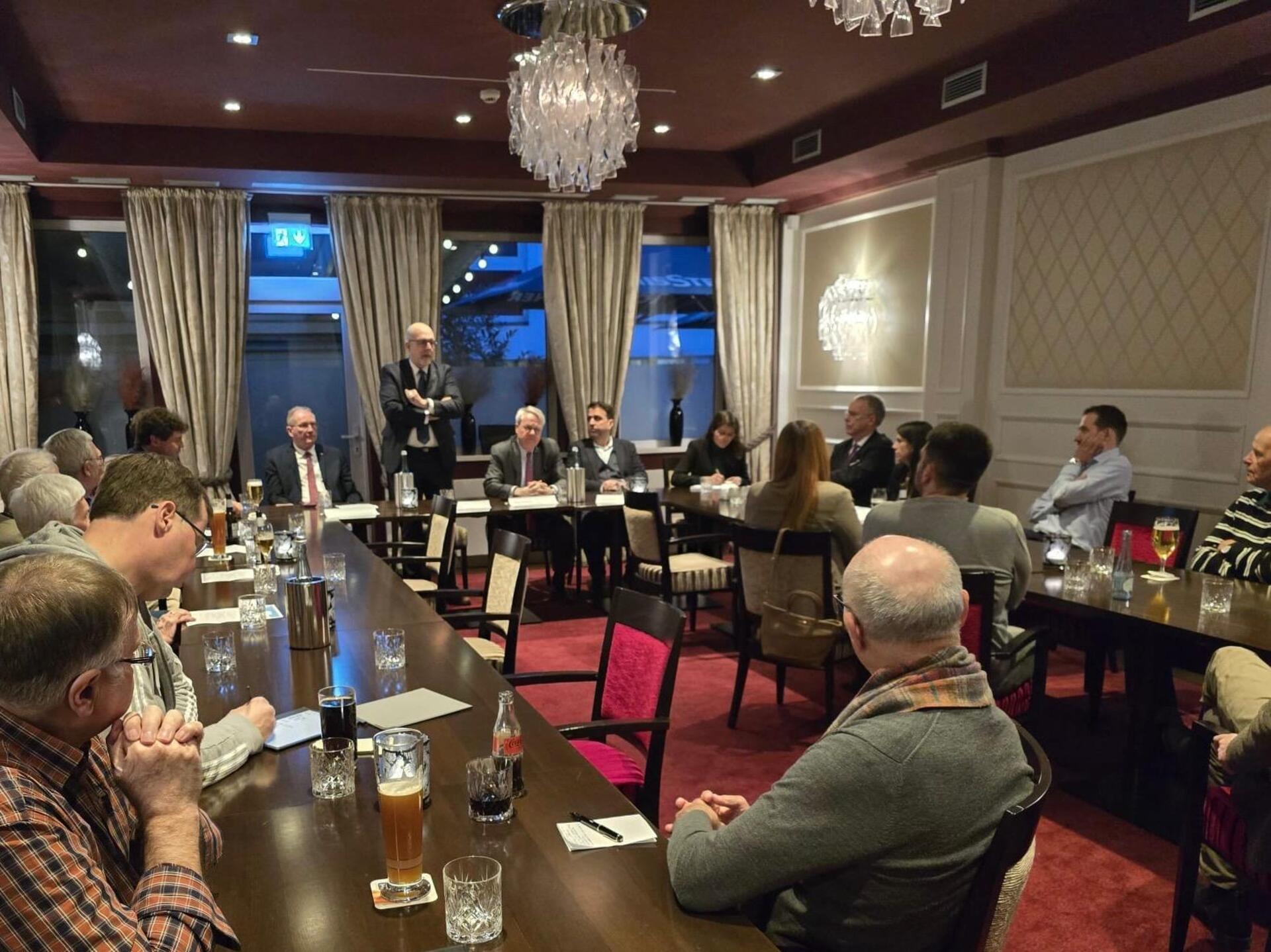 In einem Raum in einem Hotel sitzen mehrere Menschen an Tisch. Es handelt sich um einen Diskussionsabend zum Thema Energy-Port in Bremerhaven. 