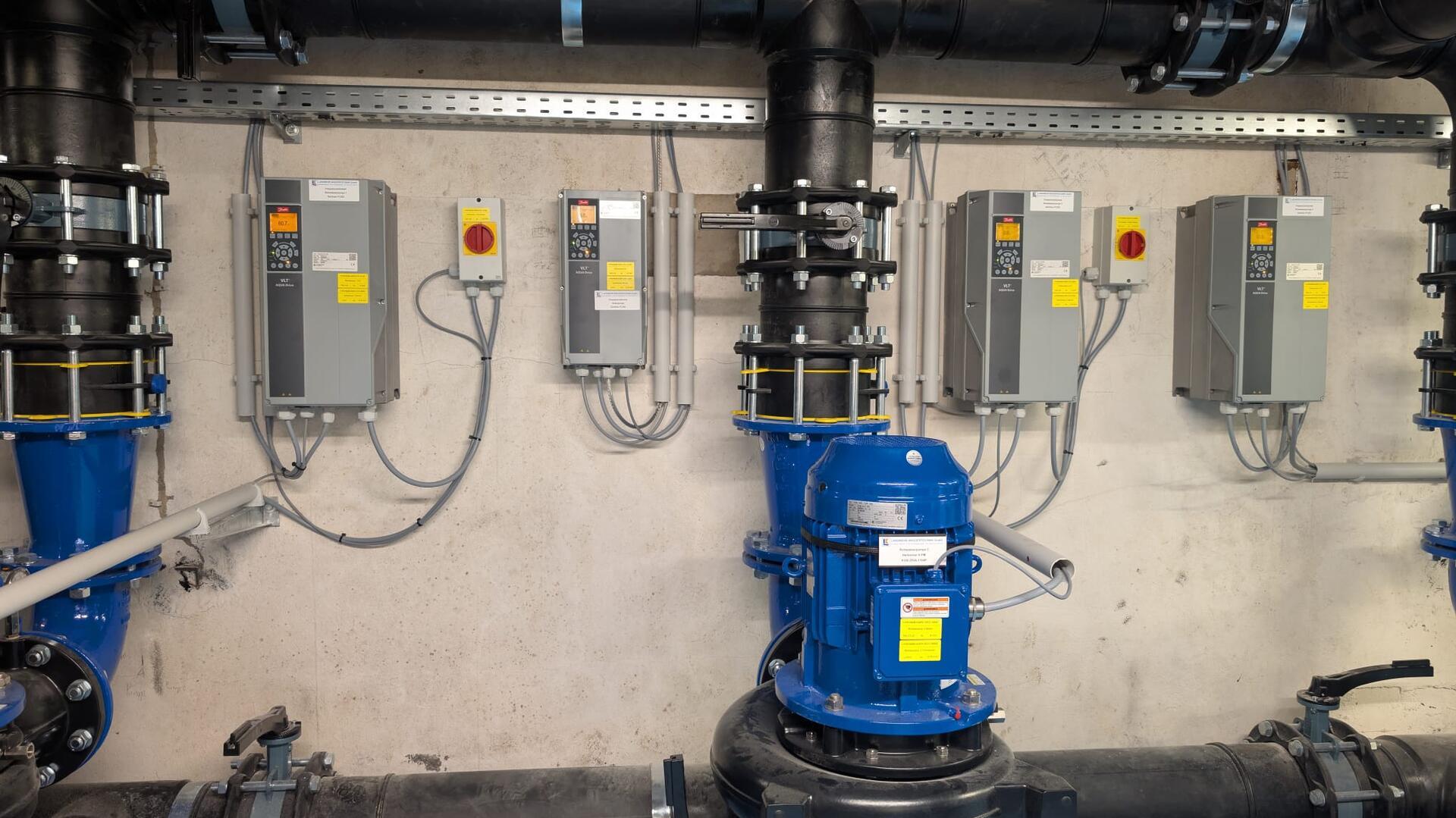Technikraum mit neu installierter, blauer Beckenwasserpumpe und moderner MSR-Technik an der Wand, bestehend aus mehreren Steuergeräten und Leitungen.