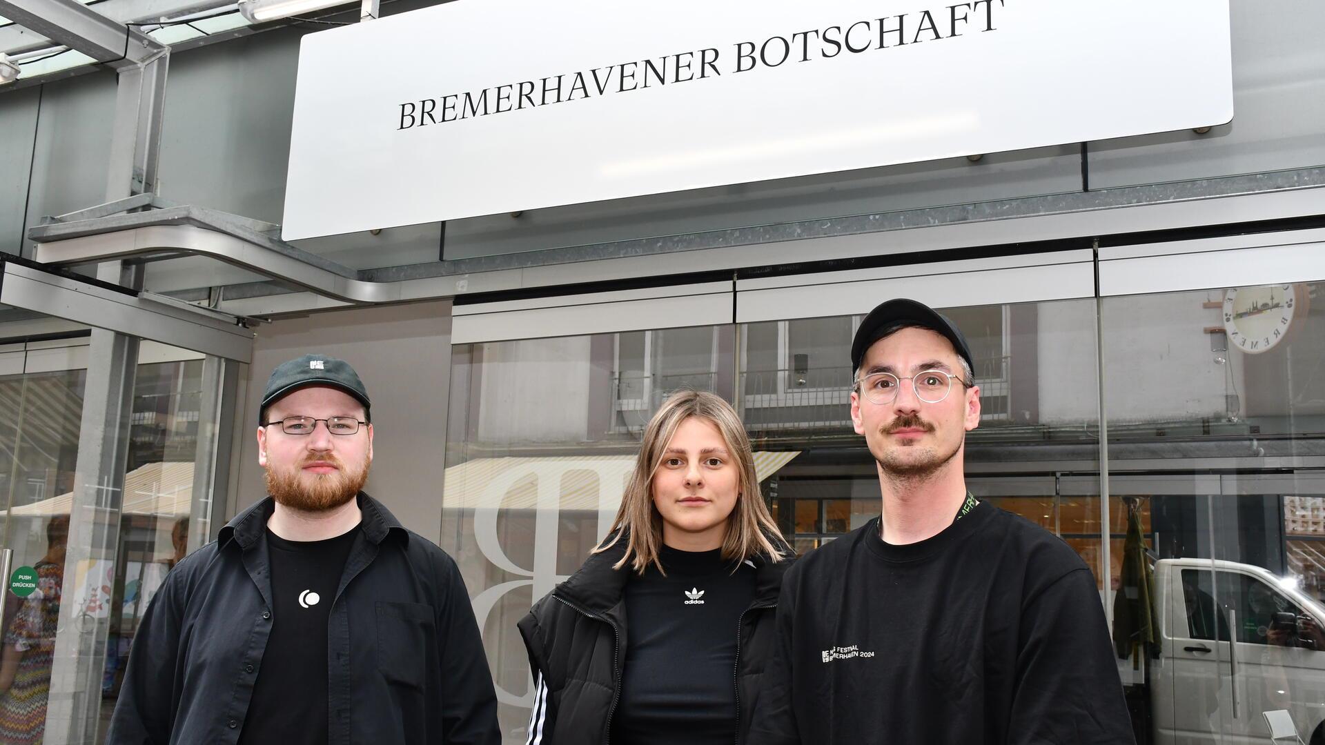 Drei Leute vor einem gläsernen Pavillon. 