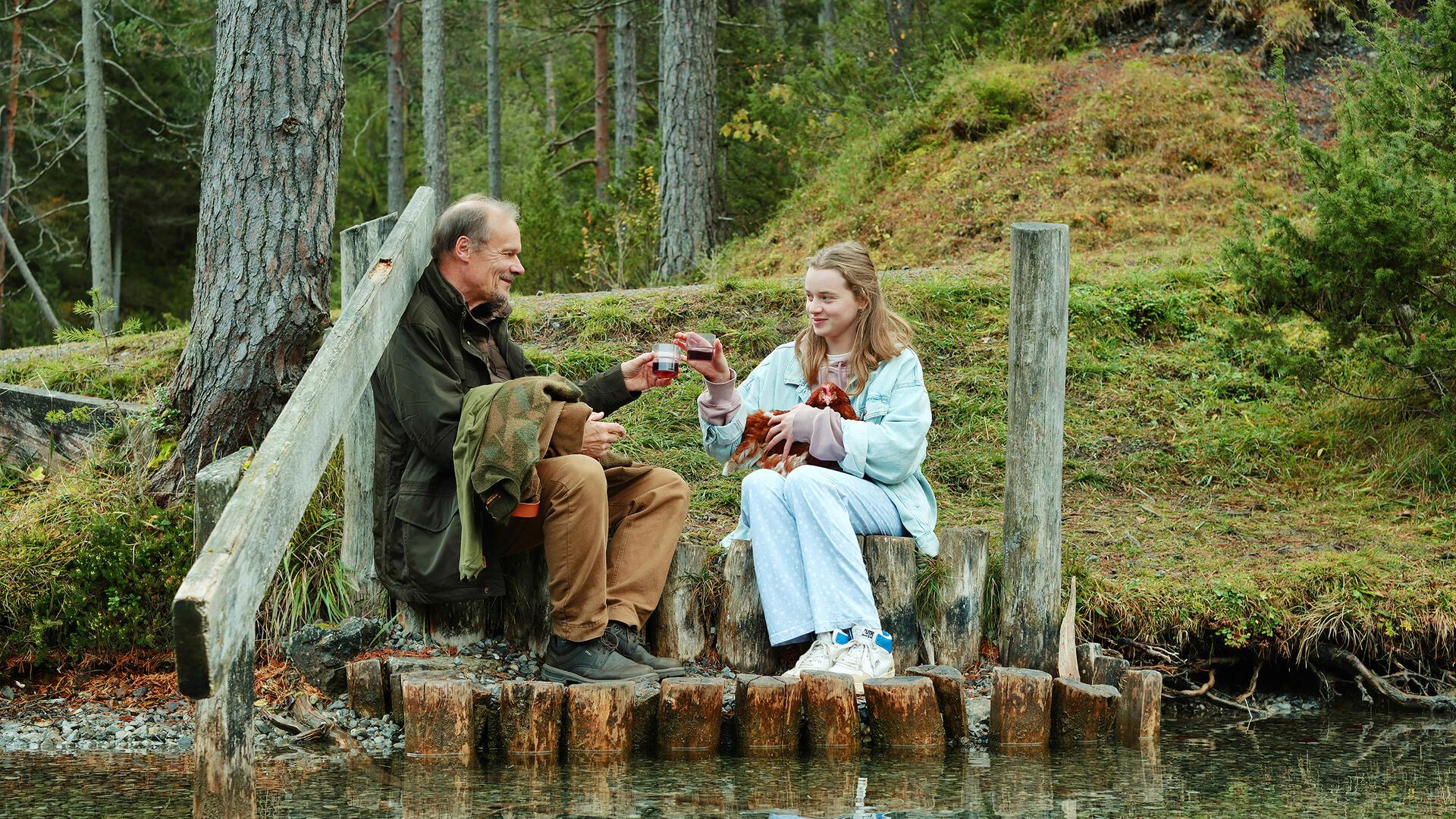 Ein Mann und eine Frau sitzen in einem Wald an einem Fluss. Edgar Selge als Helmut und Luna Wedler als Paula in einer Szene aus "Marianengraben": Das Kommunale Kino zeigt den Film am 19. März um 18 und 20.30 Uhr. Im März stehen vier weitere Filme auf dem Programm.