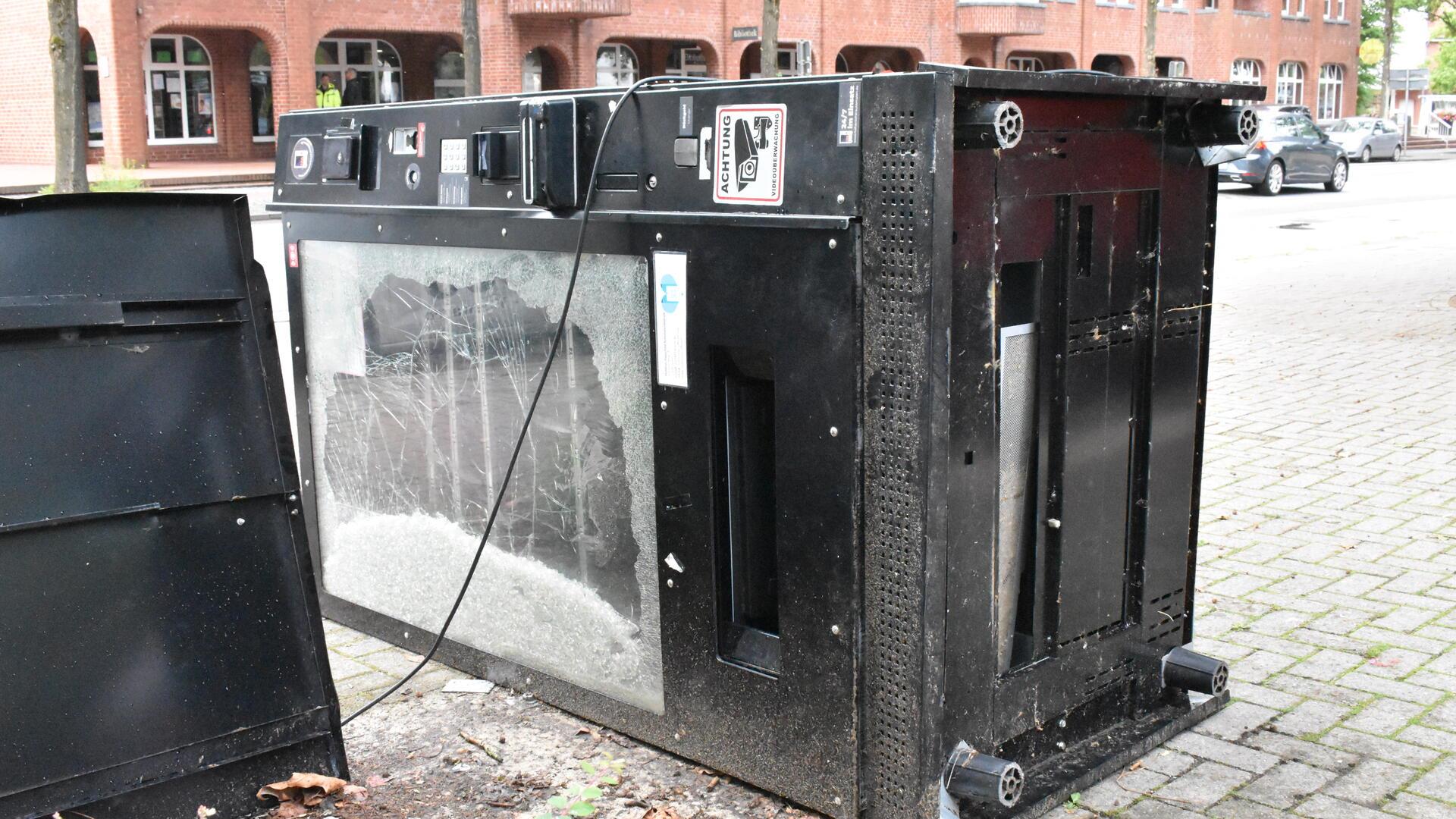 Ein zerstörter Automat liegt auf einem gepflasterten Platz.
