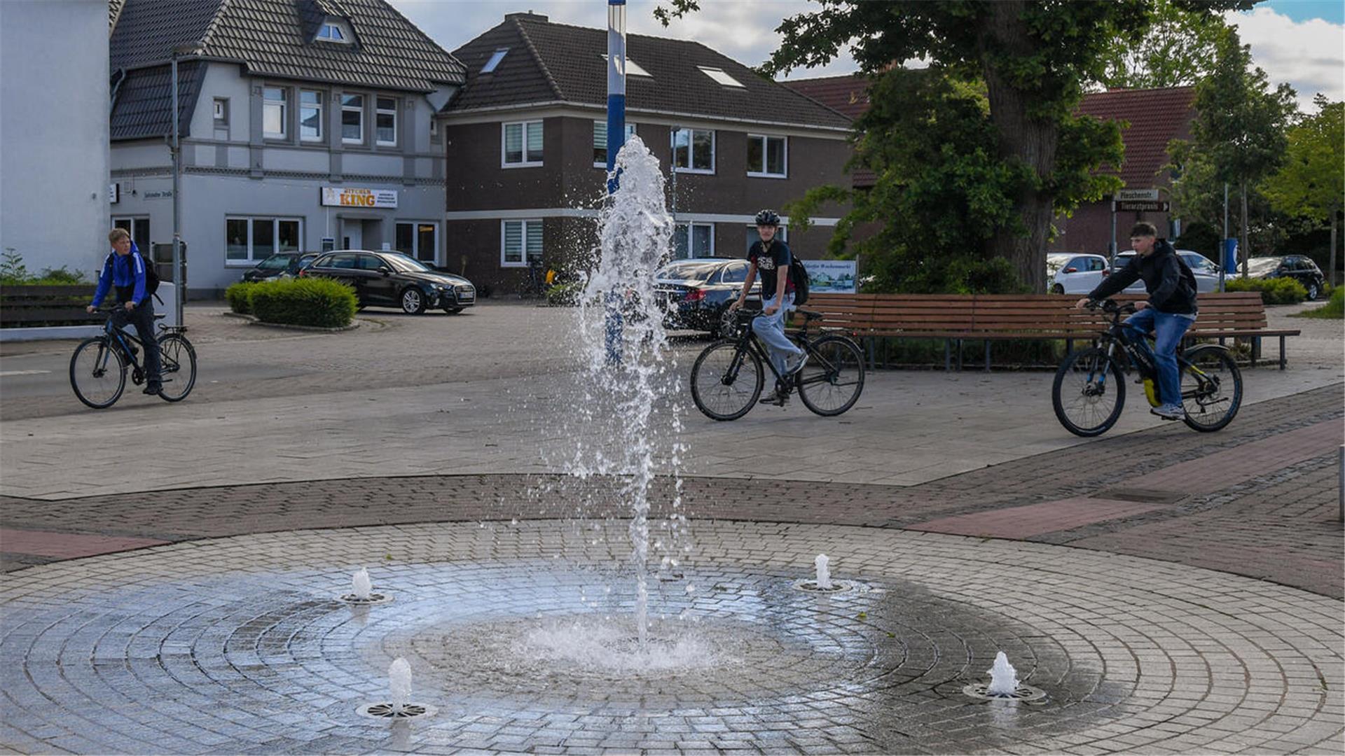 Drei junge Menschen fahren mit dem Fahrrad über einen Marktplatz.