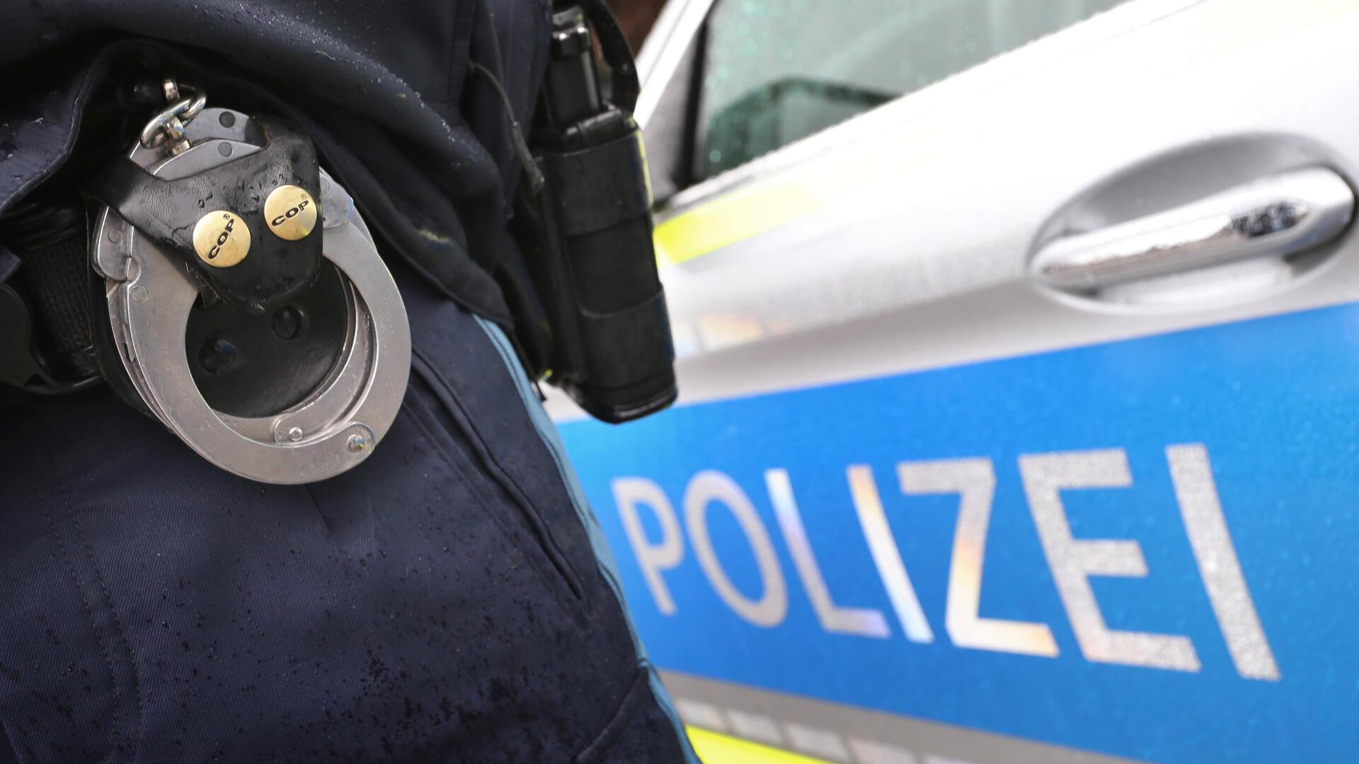  Ein Polizist mit Handschellen und einer Pistole am Gürtel steht vor einem Streifenwagen. Ein Fahrraddieb flüchtete mit einem gestohlenen Pedelec und wurde nach einer Verfolgungsjagd von der Polizei gestellt. Bei seiner Festnahme fanden die Beamten Drogen und eine fremde Krankenversichertenkarte.