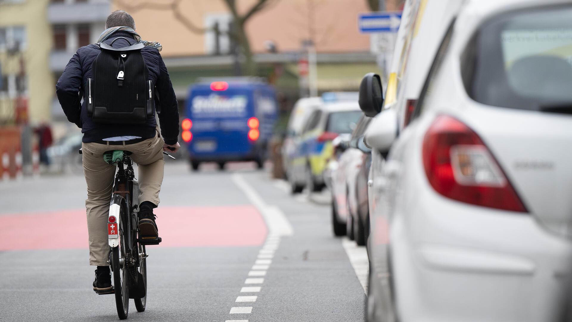 Ein Fahrradfahrer fährt auf einer Fahrradstraße an einem Schutzstreifen für geöffnete Türen an Autos vorbei.