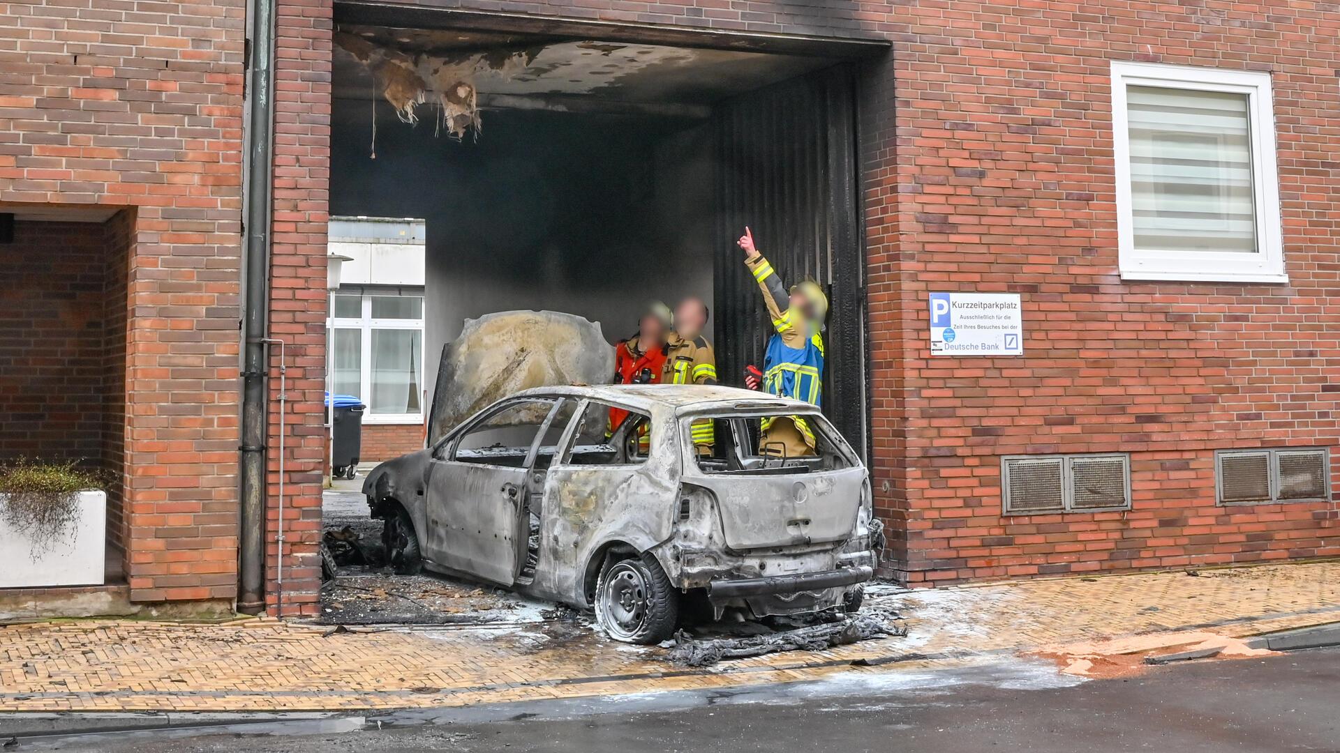 Ein brennendes Auto steht an einem Gebäude. 