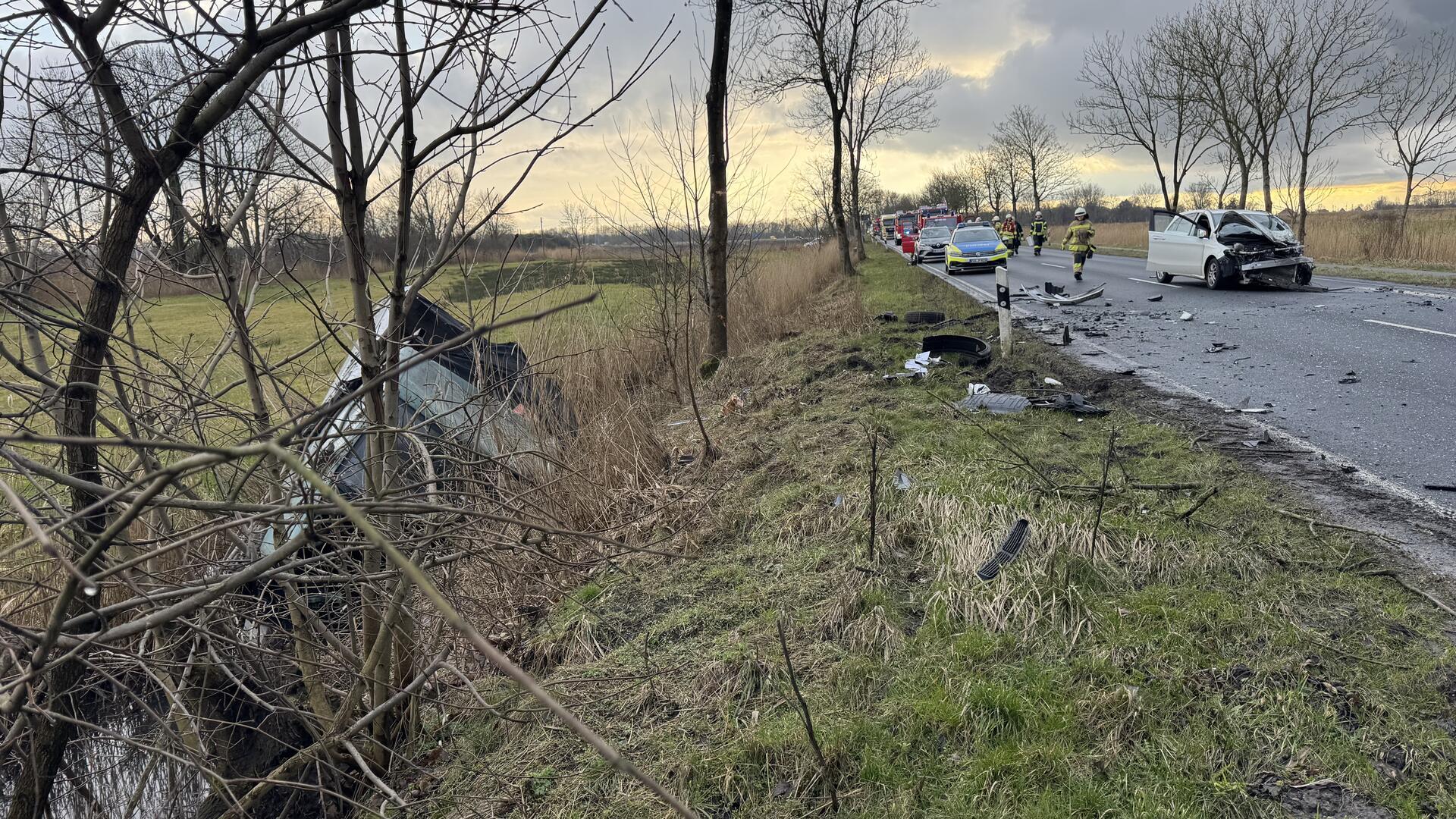 Ein zerstörtes Auto liegt in einem Graben. Auf der Straße steht ein weiteres zerstörtes Auto.
