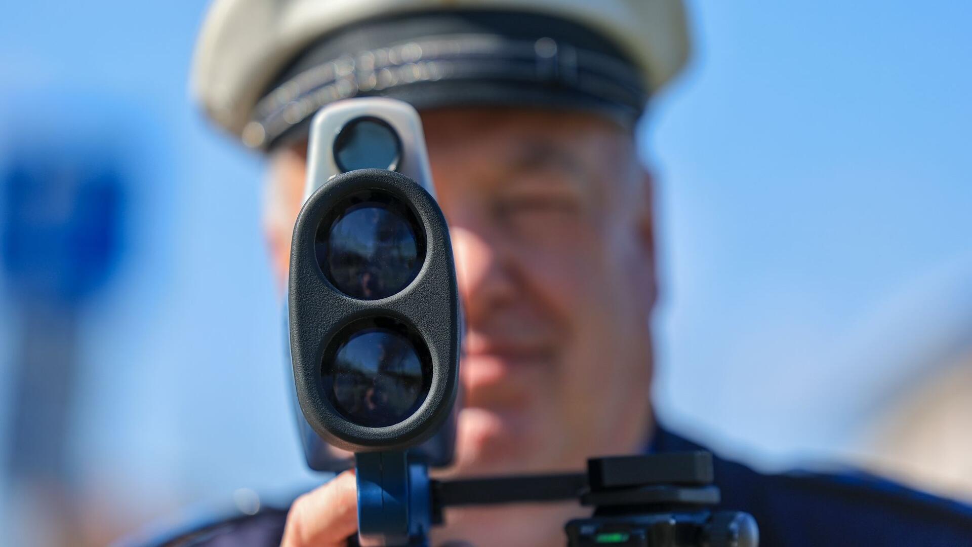 Ein Polizist misst mit einem Laserhandmessgerät (Laserpistole) während einer Geschwindigkeitskontrolle einen Autofahrer.