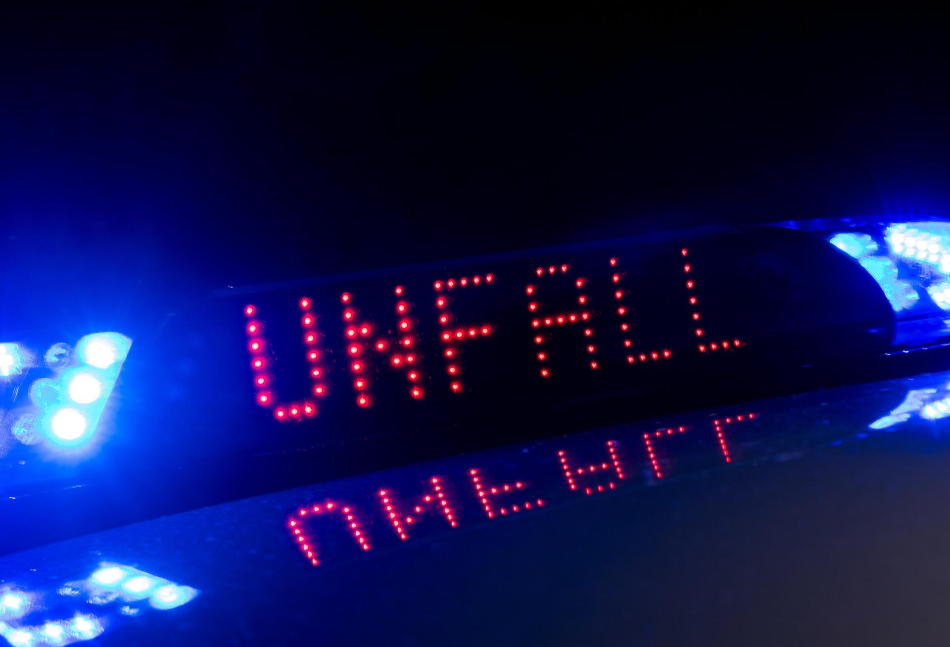 Das Blaulicht auf einem Fahrzeug der Polizei leuchtet in der Dunkelheit, während auf dem Display der Hinweis «Unfall» zu lesen ist.
