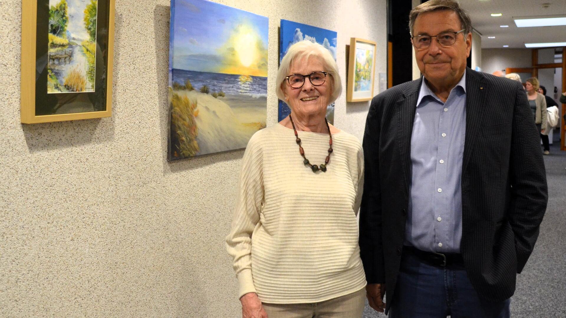 Eine Frau und ein Mann stehen vor mehreren an einer Wand aufgehängten Bildern