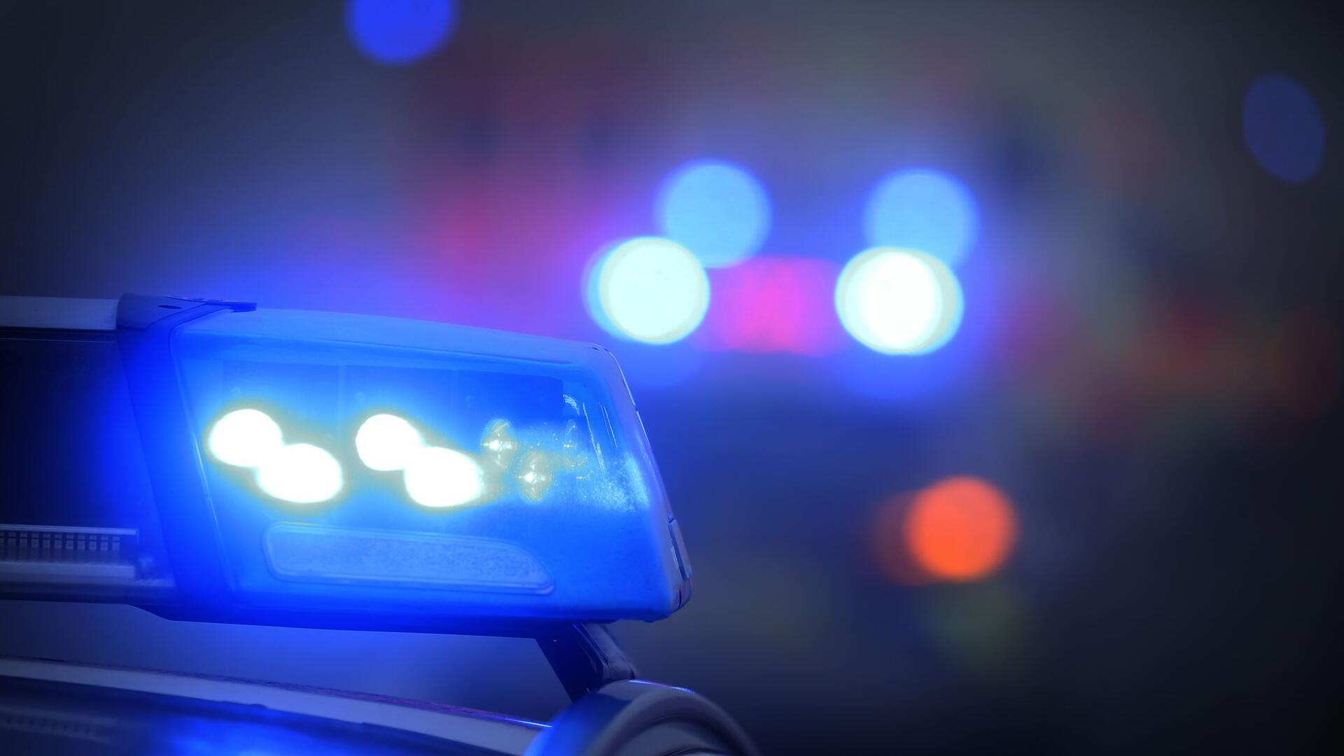 Ein Polizeiauto mit eingeschaltetem Blaulicht steht an einer Straße.