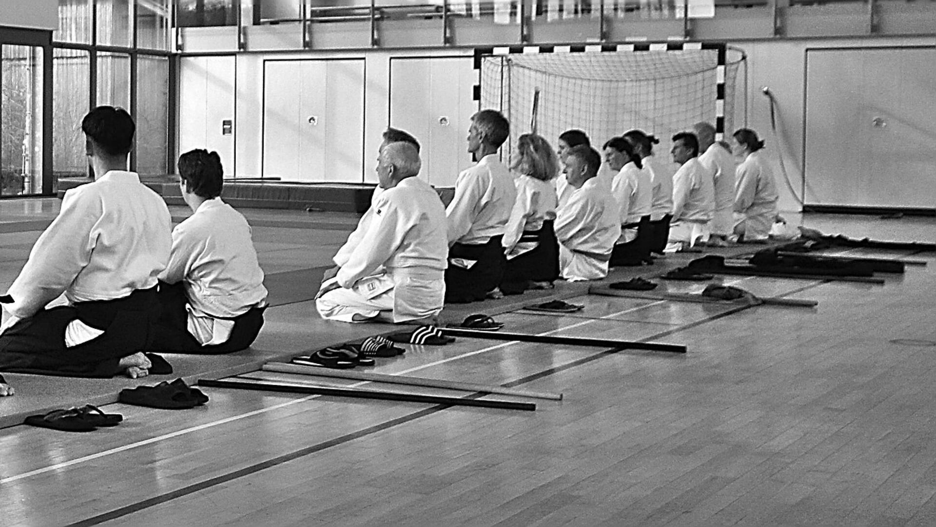 Eine Gruppe Kampfsportler sitzt auf Knien in der Sporthalle