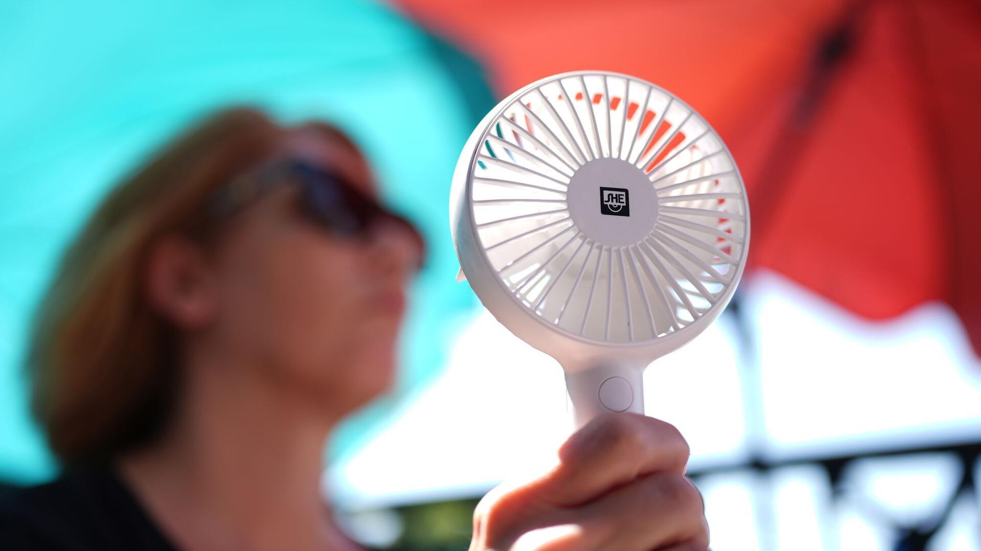 Eine Frau kühlt sich mit einem Handventilator in der Mittagssonne ab. Für Juli und August sagen Meteorologen einen heißen und trockenen Sommer voraus.