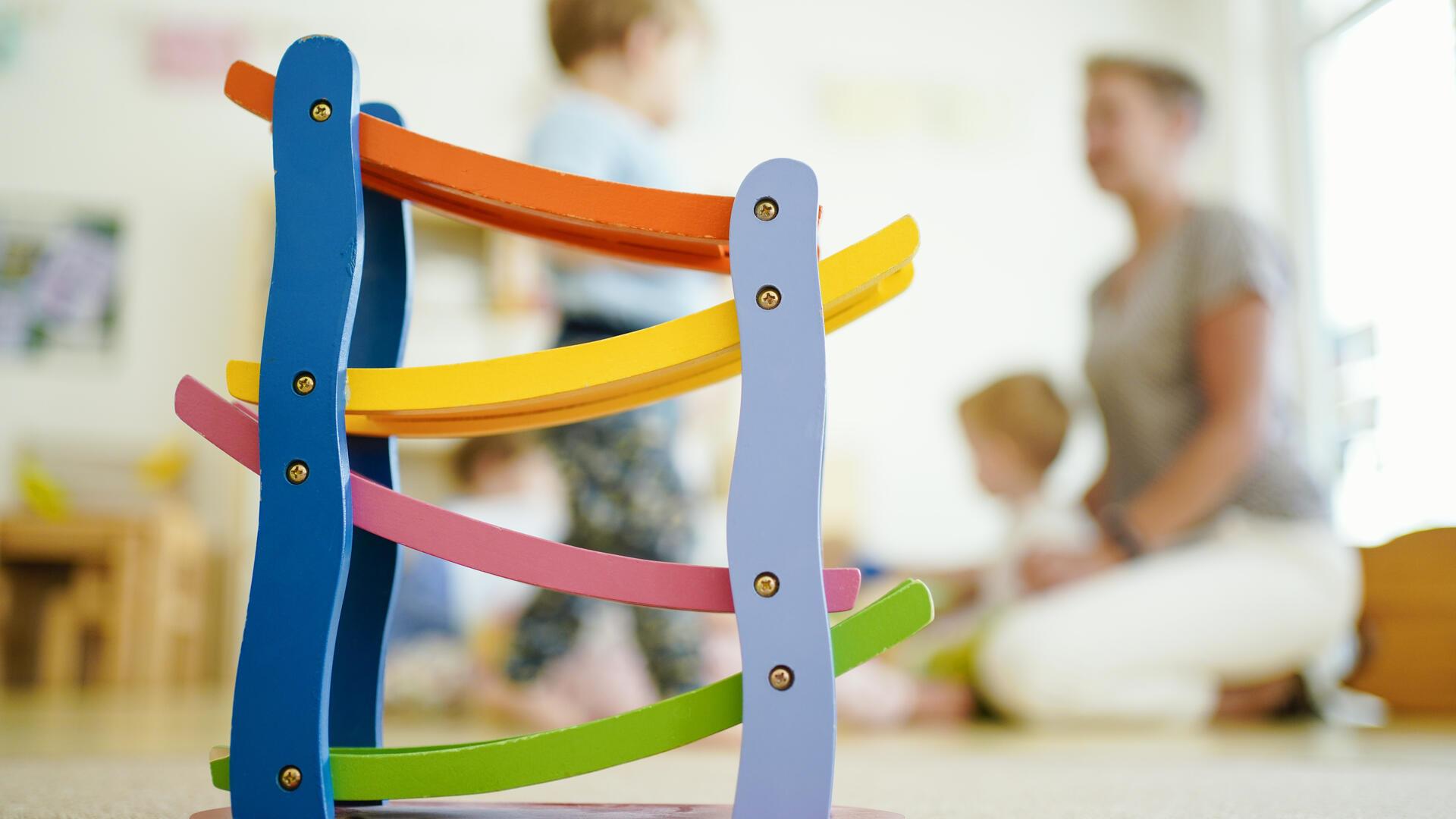 Eine Erzieherin spielt in einer Kindertagesstätte hinter einer Rollbahn mit Kindern.Eine Studie zeigt: Viele Erzieherinnen und Erzieher verlassen den Beruf früh oder reduzieren ihre Stunden. Nur ein Drittel bleibt auch nach zehn Jahren in der Kindertagesbetreuung im Land Bremen tätig.