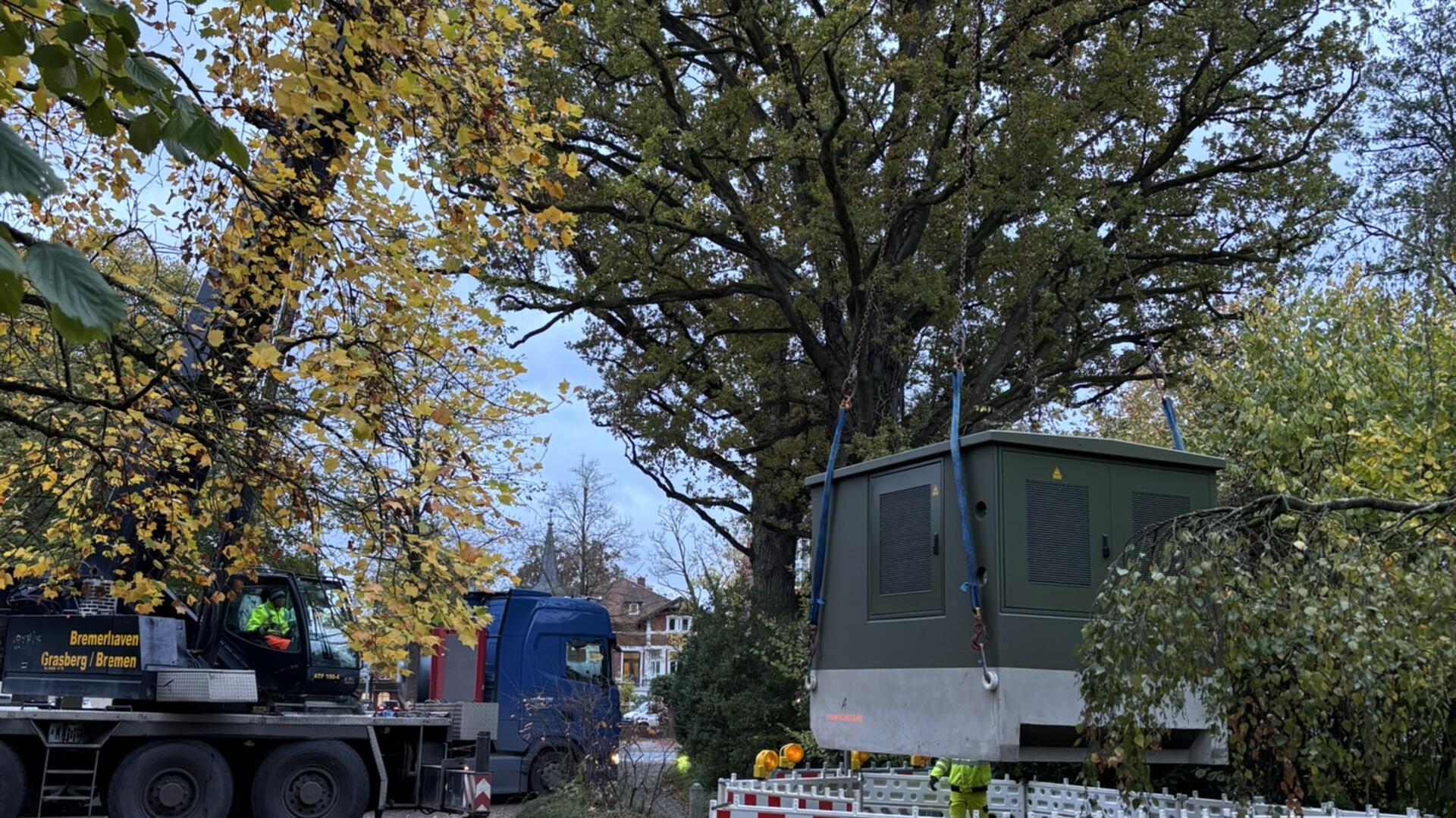 Dunkelgrüne Trafostation wird mit Kran von Lkw gehoben.