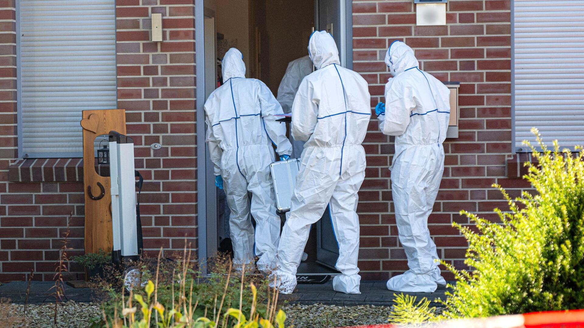 Männer in weißen Kitteln betreten ein Haus