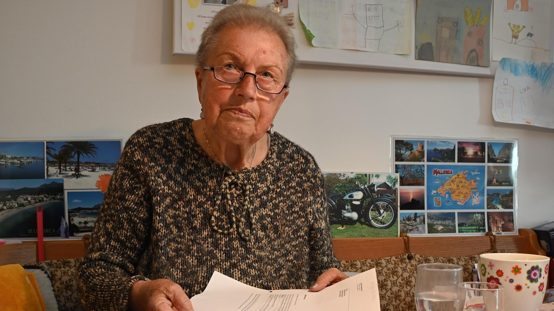 Eine Frau mit Brille. Sie sitzt an einem Tisch und zeigt die Zettel in die Kamera.