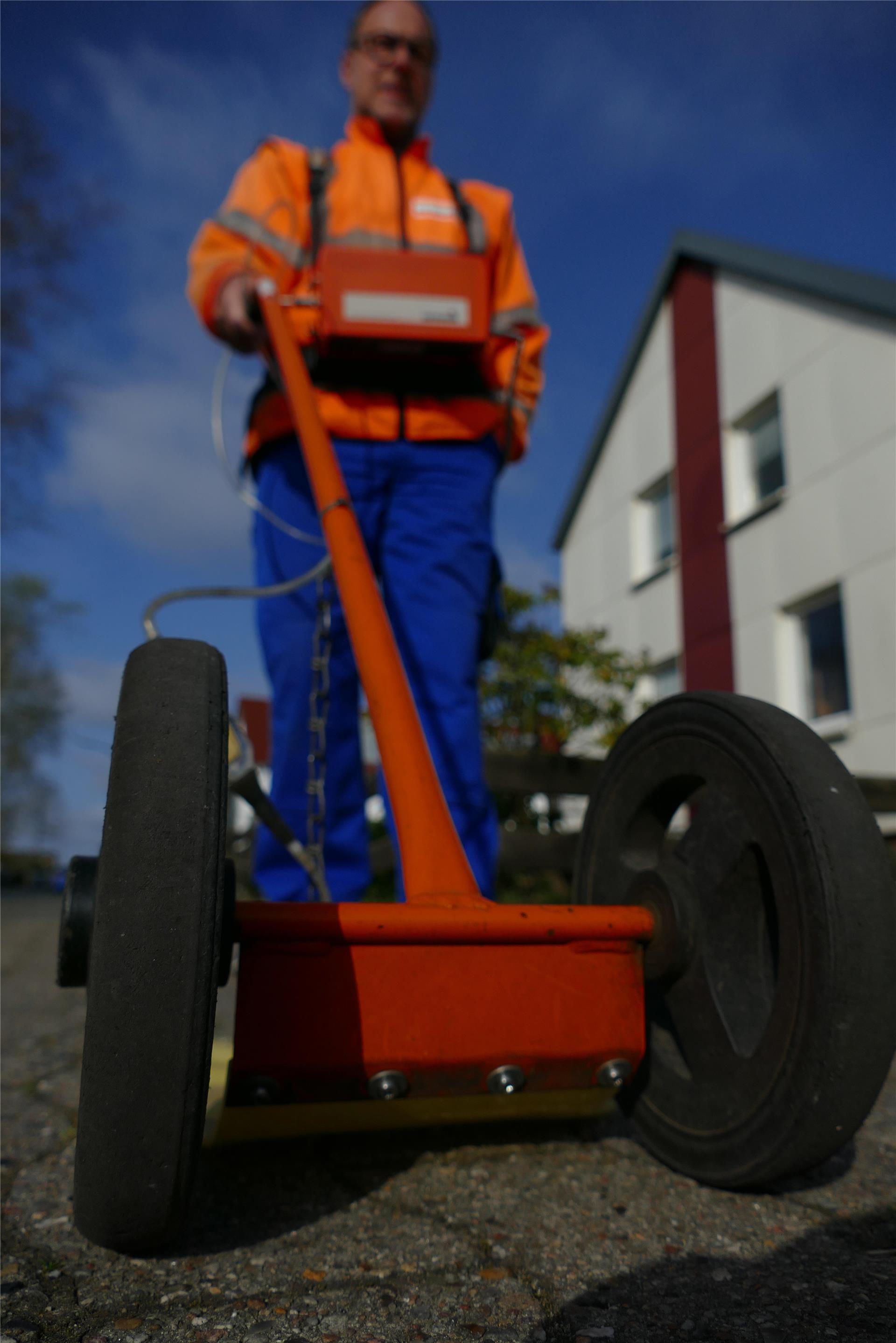 Ein Mann in Arbeitsbekleidung schiebt ein Gerät auf Gummirädern vor sich her, das kleinste Undichtigkeiten in Gasleitungen aufspüren soll.  