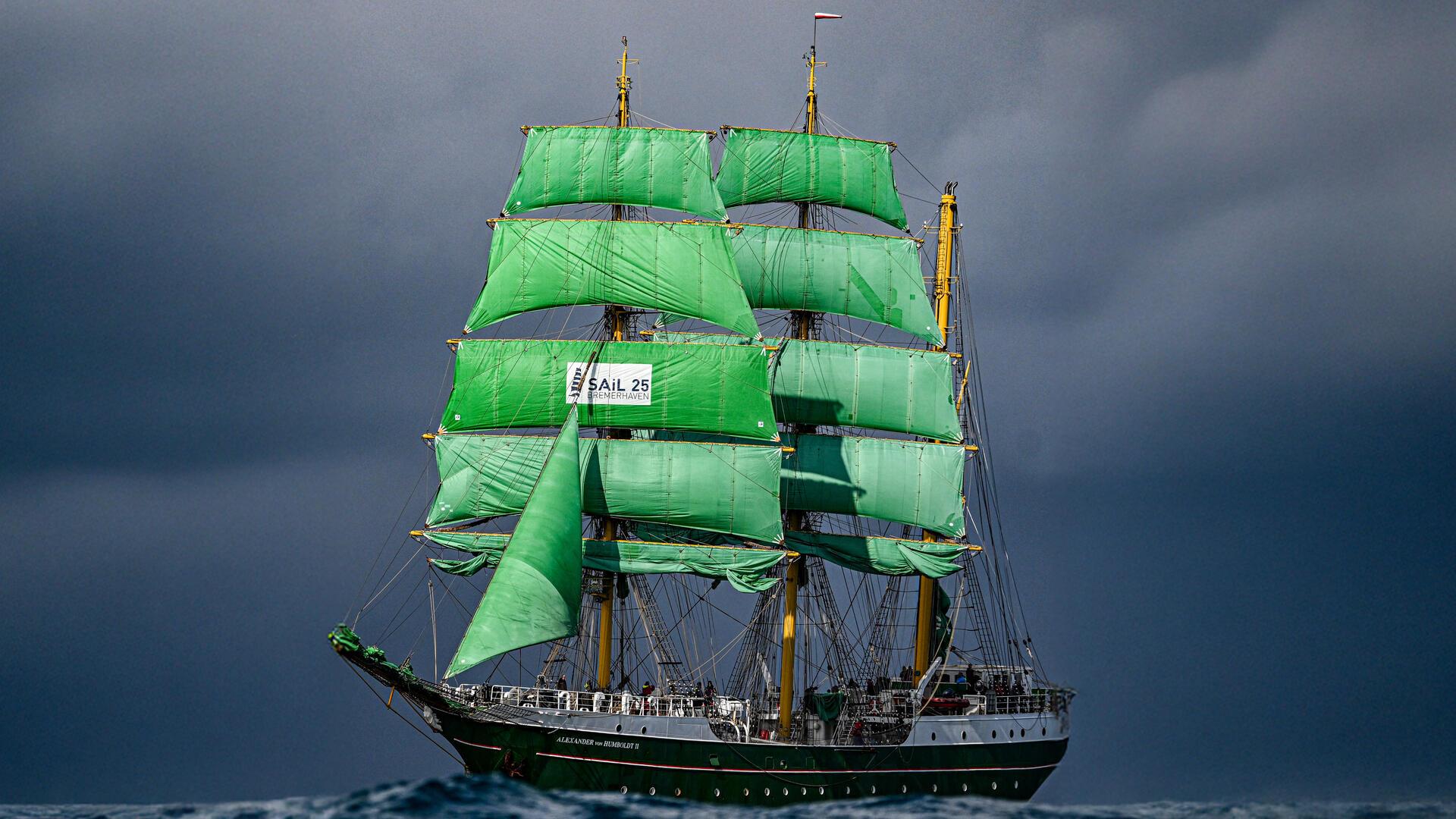 Ein Segelschiff mit grünen Segeln auf hoher See vor dramatischem Himmel.