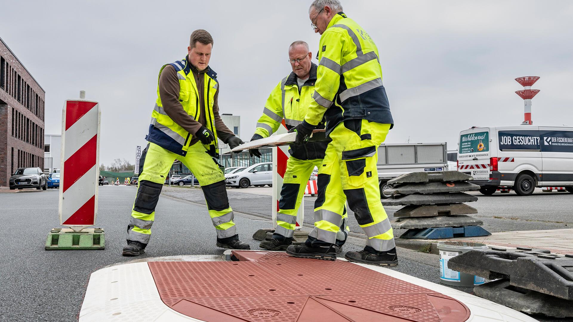 Drei Männer bringen ein Platte auf einer Straße in Position.