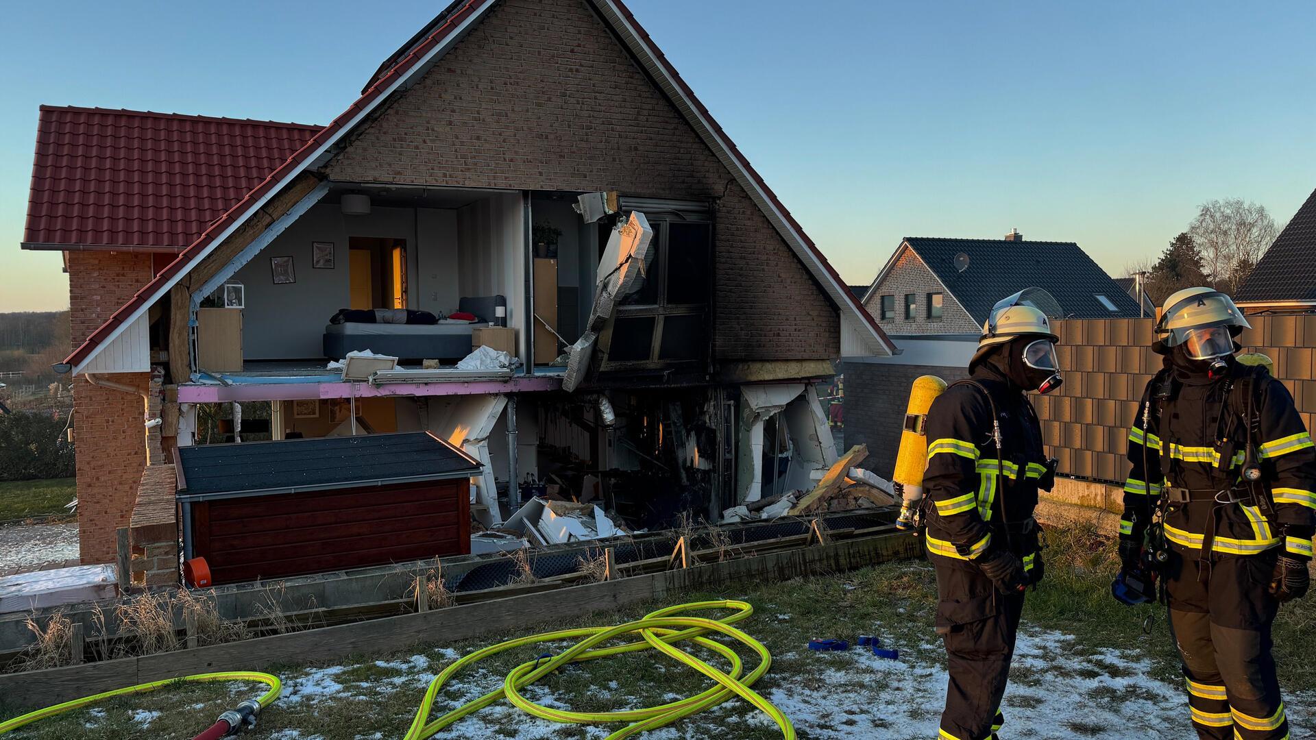 Feuerwehrleute stehen vor einem beschädigten Wohnhaus. Bei der Explosion in einem Wohnhaus in Schönberg (Kreis Herzogtum Lauenburg) ist eine Hauswand abgebrochen. Es explodierte offenbar ein Solarstromspeicher und riss Fenster und einen Teil der Wand heraus. Verletzt wurde niemand, wie ein Sprecher des Lagezentrums in Lübeck sagte. 