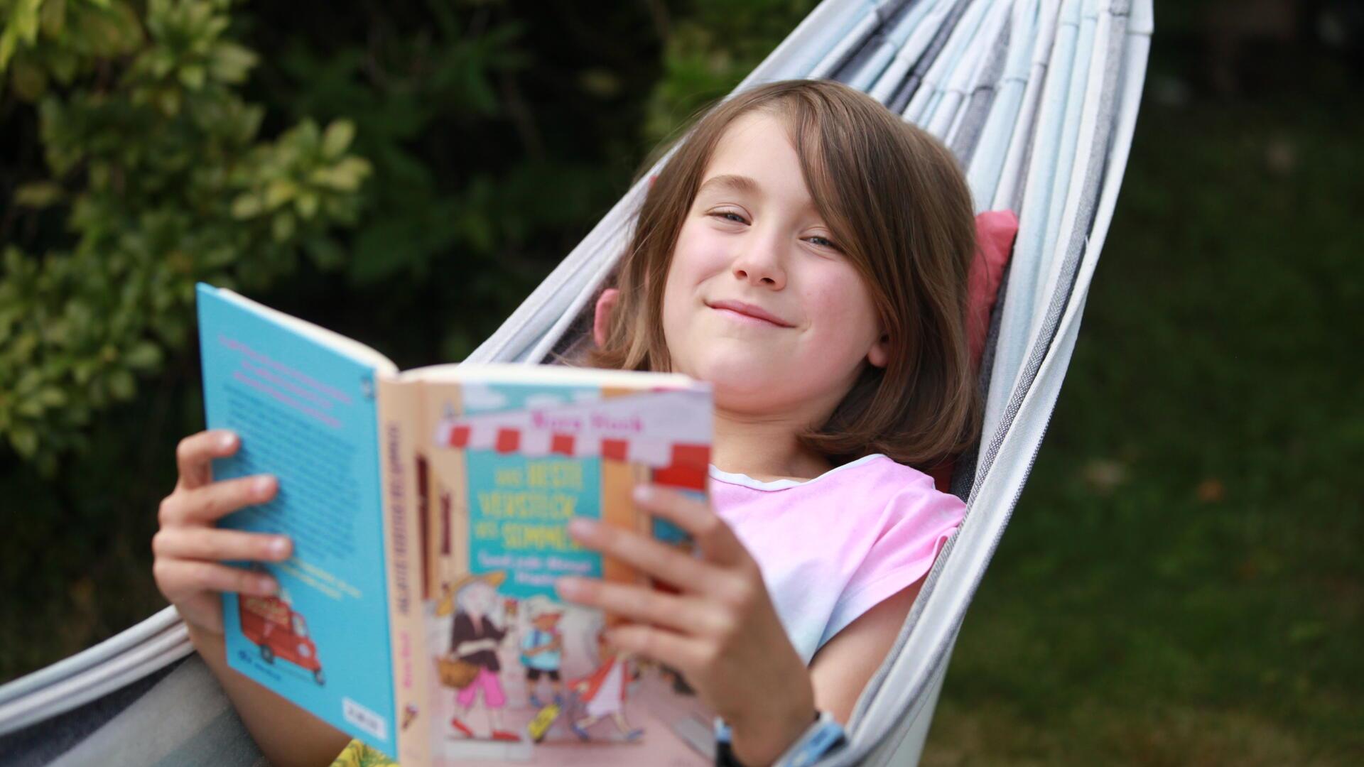 Ein Kind in einer Hängematte liest ein Buch und lächelt
