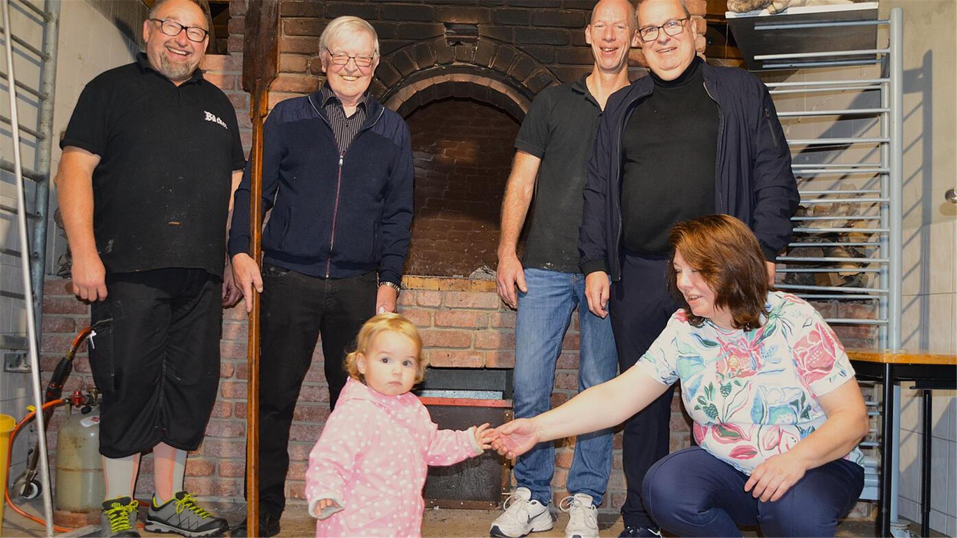 Vier Männer, eine Frau und ein Kind stehen vor einem Steinbackofen.
