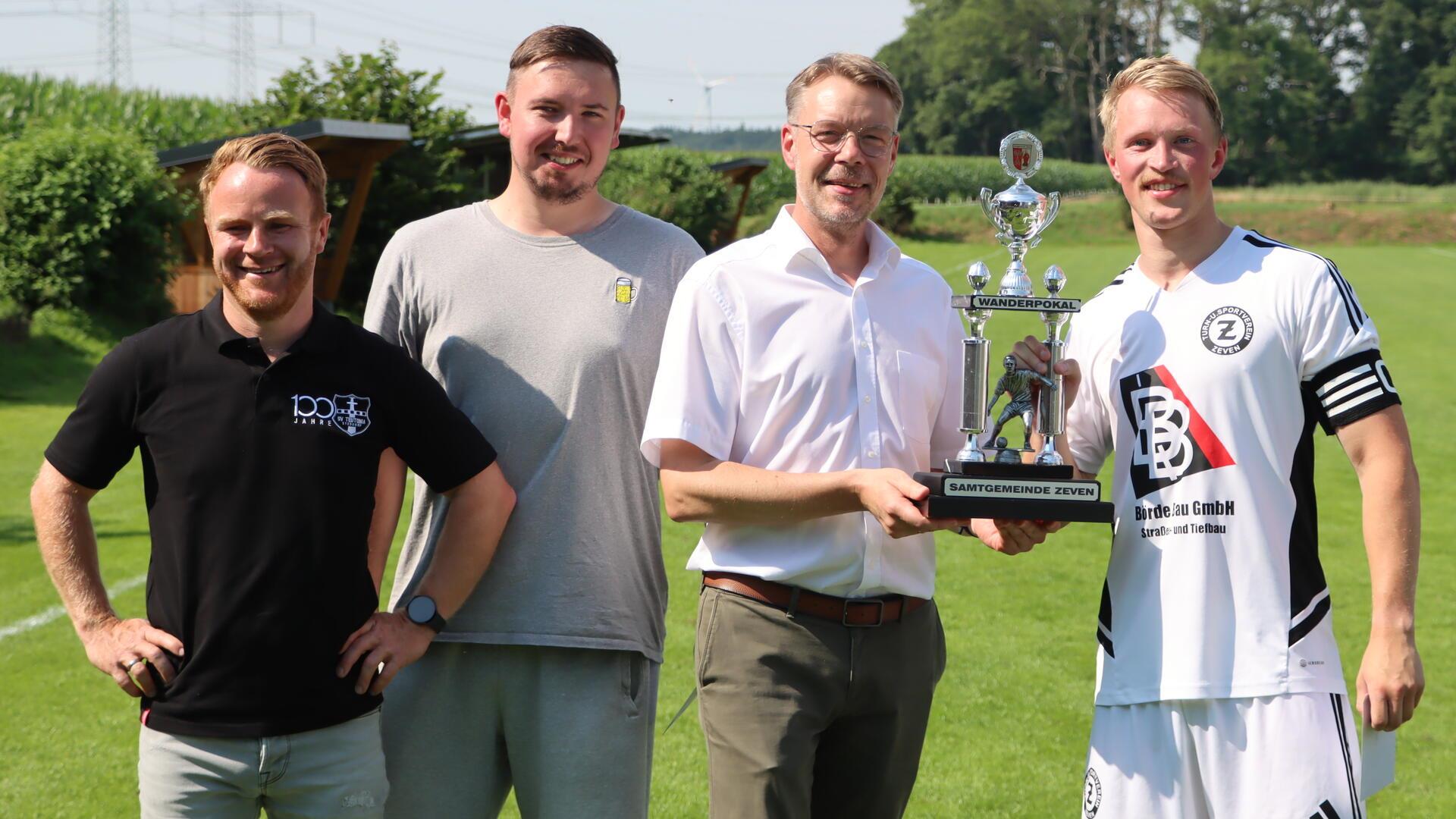 TuS Zeven gewinnt mit 2:0-Sieg gegen Steddorf erneut den Samtgemeindepokal Fröhliche Gesichter bei der Siegerehrung (von links): Teutonia-Vorsitzender Marco Hargens, zweiter Vorsitzender Florian Schäfer, Samtgemeinde-Bürgermeister Henning Fricke und Mannschaftsführer Lukas Huß.