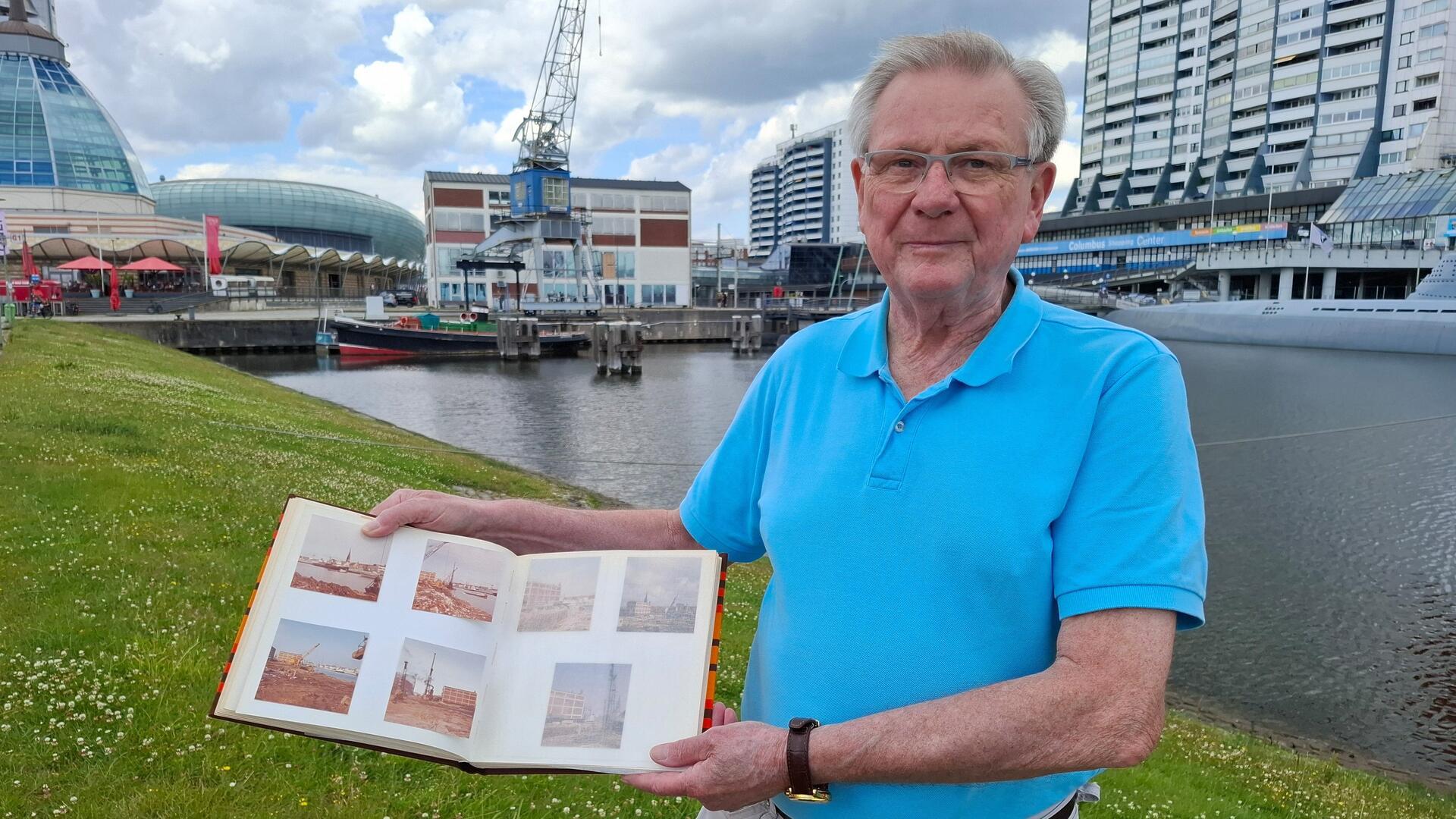 Ein Mann steht mit einem Fotoalbum auf der Rasenböschung am Alten Hafen am Alten Hafen